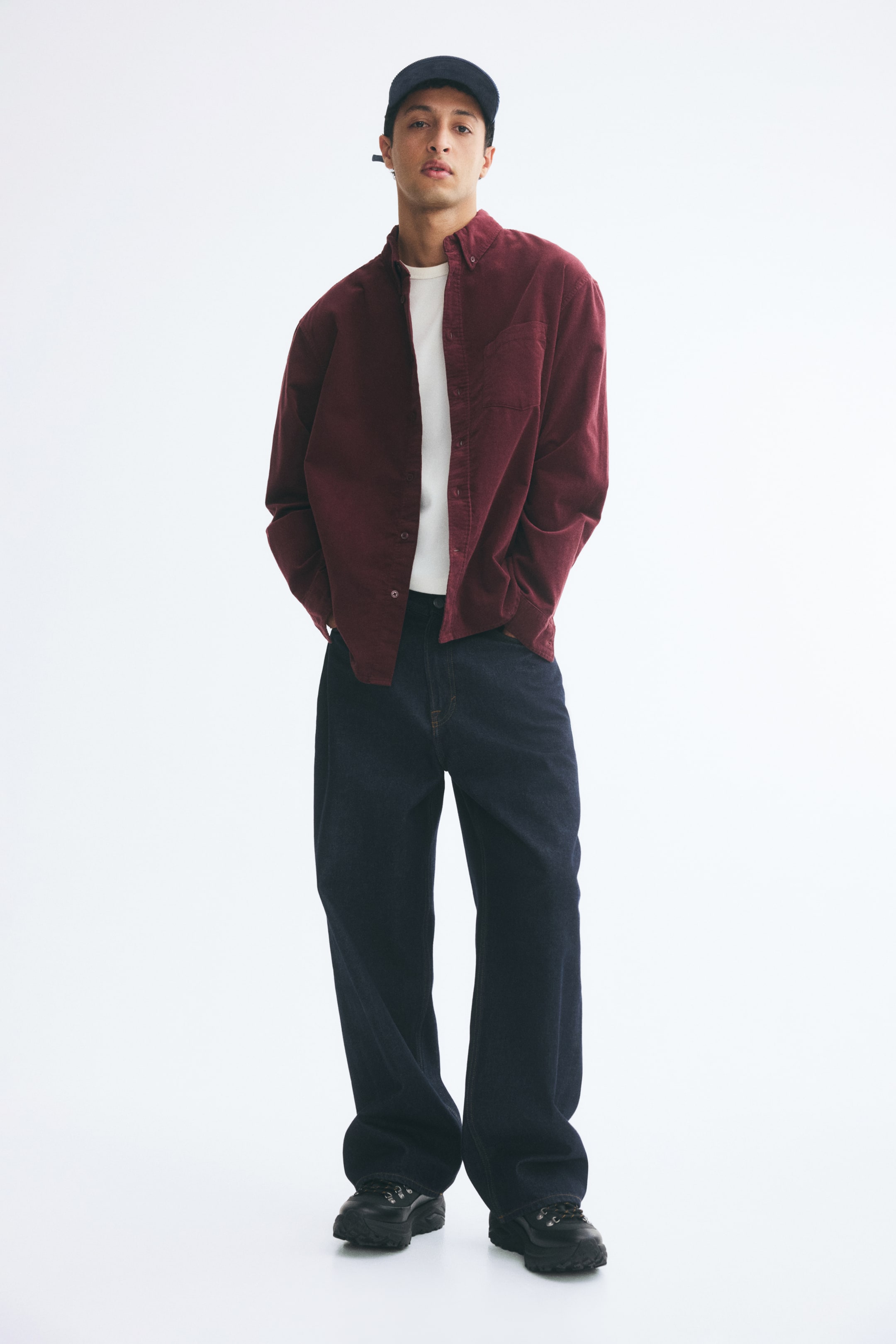 Grotere afbeelding bekijken: Een bordeauxrode corduroy overhemd van katoen wordt open gedragen door het model over een wit T-shirt en gecombineerd met een donkere jeans met wijde pijpen. Het overhemd met lange mouwen heeft een button-downkraag, één borstzak en een regular fit.