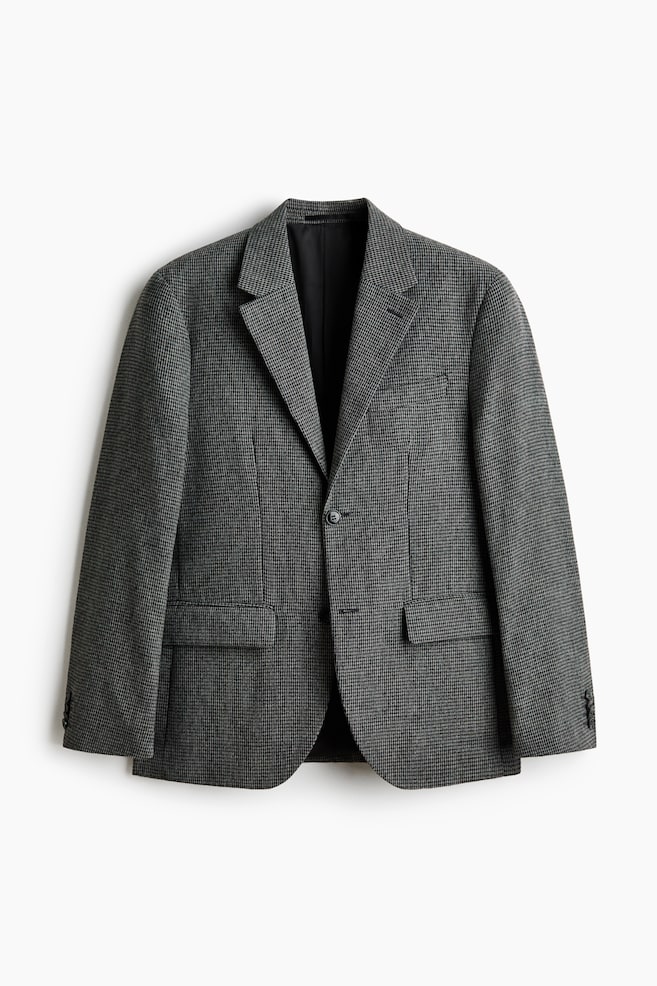 A grey and black houndstooth blazer is shown from the front, featuring notch lapels, a single-button closure, a welt chest pocket, and two flap pockets. Each sleeve cuff is displaying three buttons. - 1