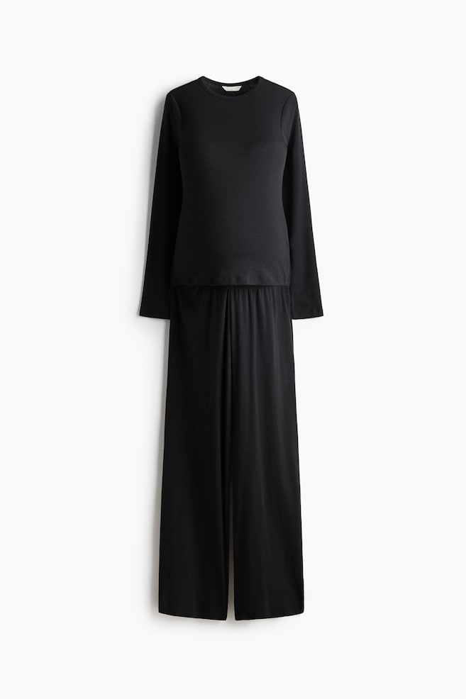 A black pyjama set is presenting from the front, featuring a long-sleeved top with a round neckline and long bottoms with an elasticated waist. - 1