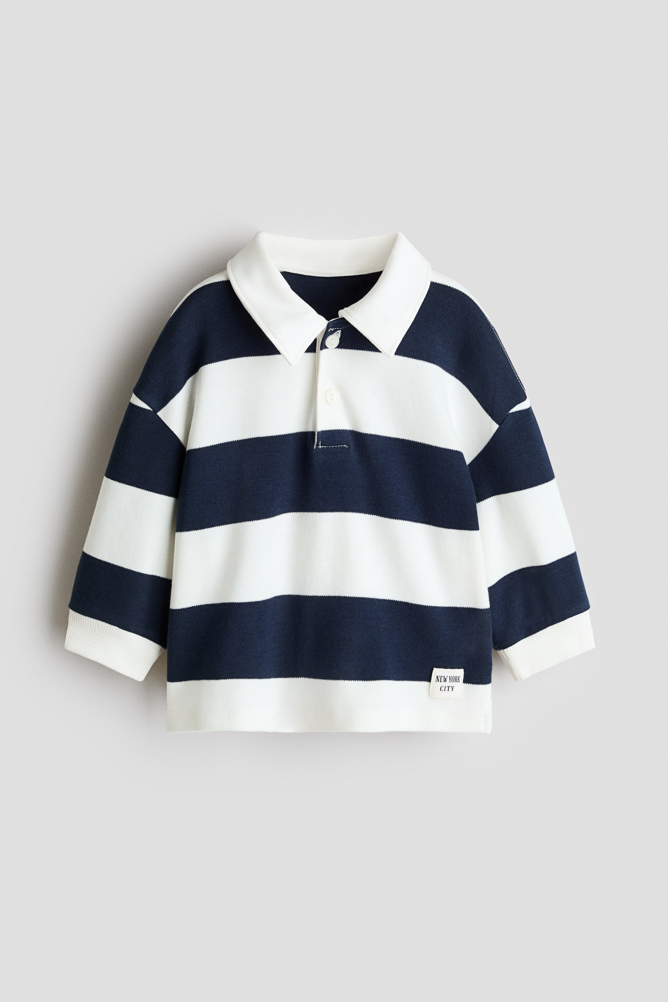 View larger image: A long-sleeved rugby shirt showcasing navy blue and white horizontal stripes, complemented by a white pointed collar and a two-button placket with white buttons. It also features white ribbed cuffs and a small "NEW YORK CITY" label on the lower front.