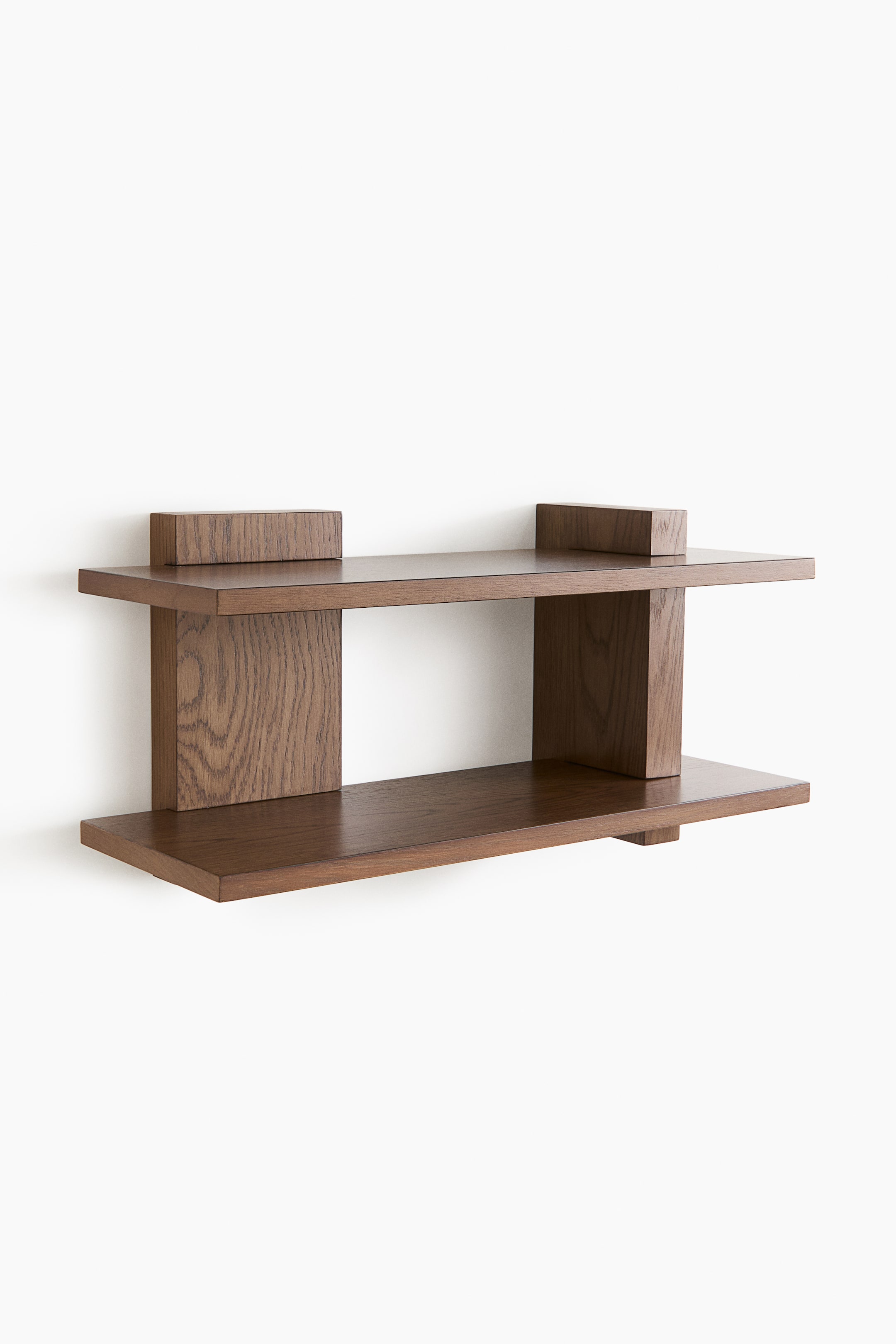 Grotere afbeelding bekijken: Een donkerbruine houten wandplank heeft twee horizontale planken in een modern, open design en is frontaal afgebeeld. De bovenste plank is voorzien van twee kleine, verhoogde rechthoekige blokken, en de onderste plank ondersteunt de bovenste met twee verticale houten panelen.