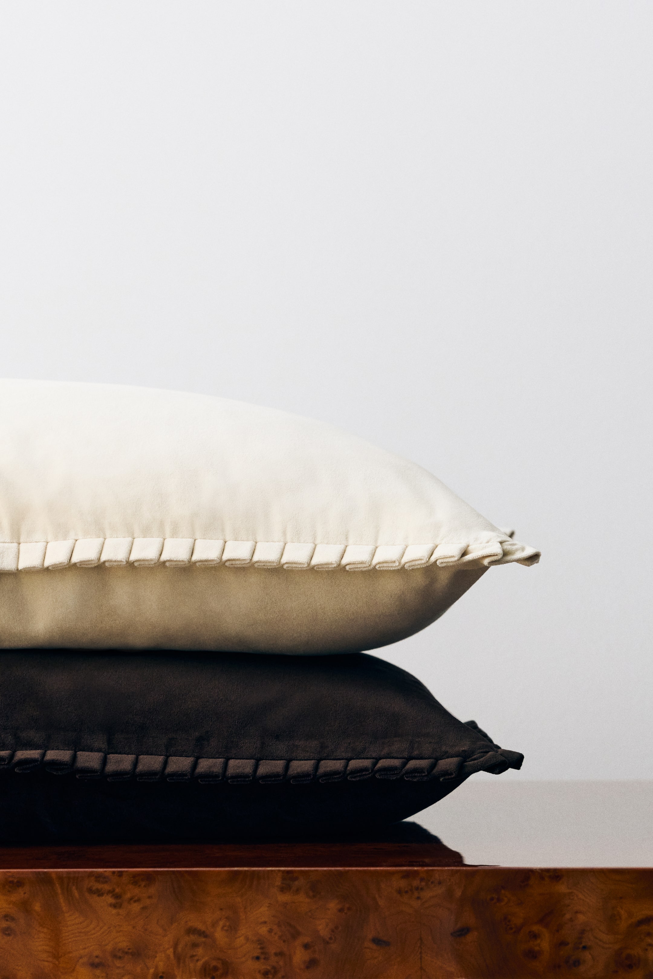 View larger image: Two rectangular cushion covers in soft cotton velvet are resting in a stack, with a cream-coloured cover sitting on top of a dark brown cover. Both covers feature a detailed pleated border along their edges, highlighting their soft, velvety texture.