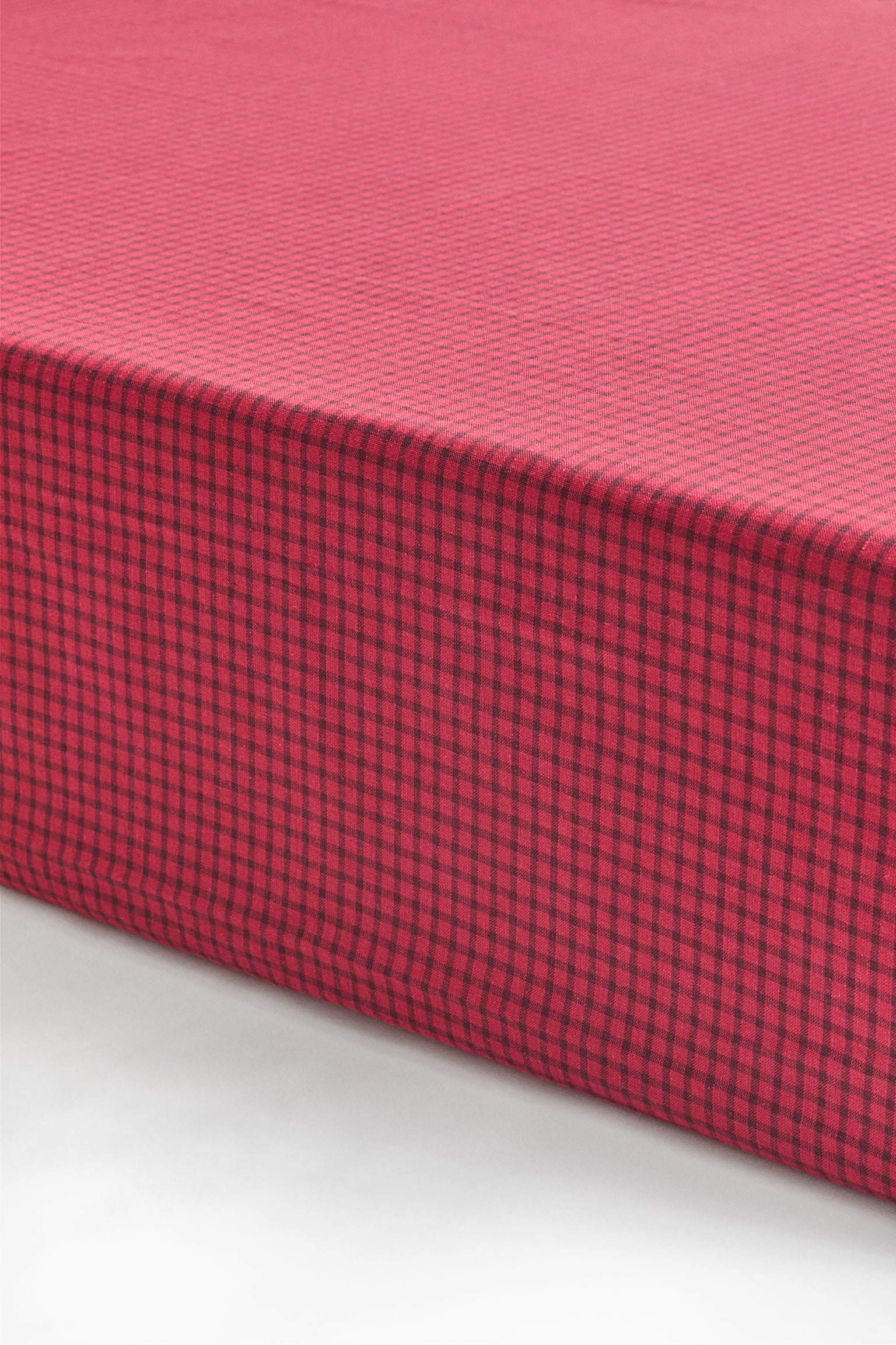 A fitted sheet featuring a red and black gingham pattern is covering a mattress corner, showing a smooth, taut fit along the top and side edges. - 1