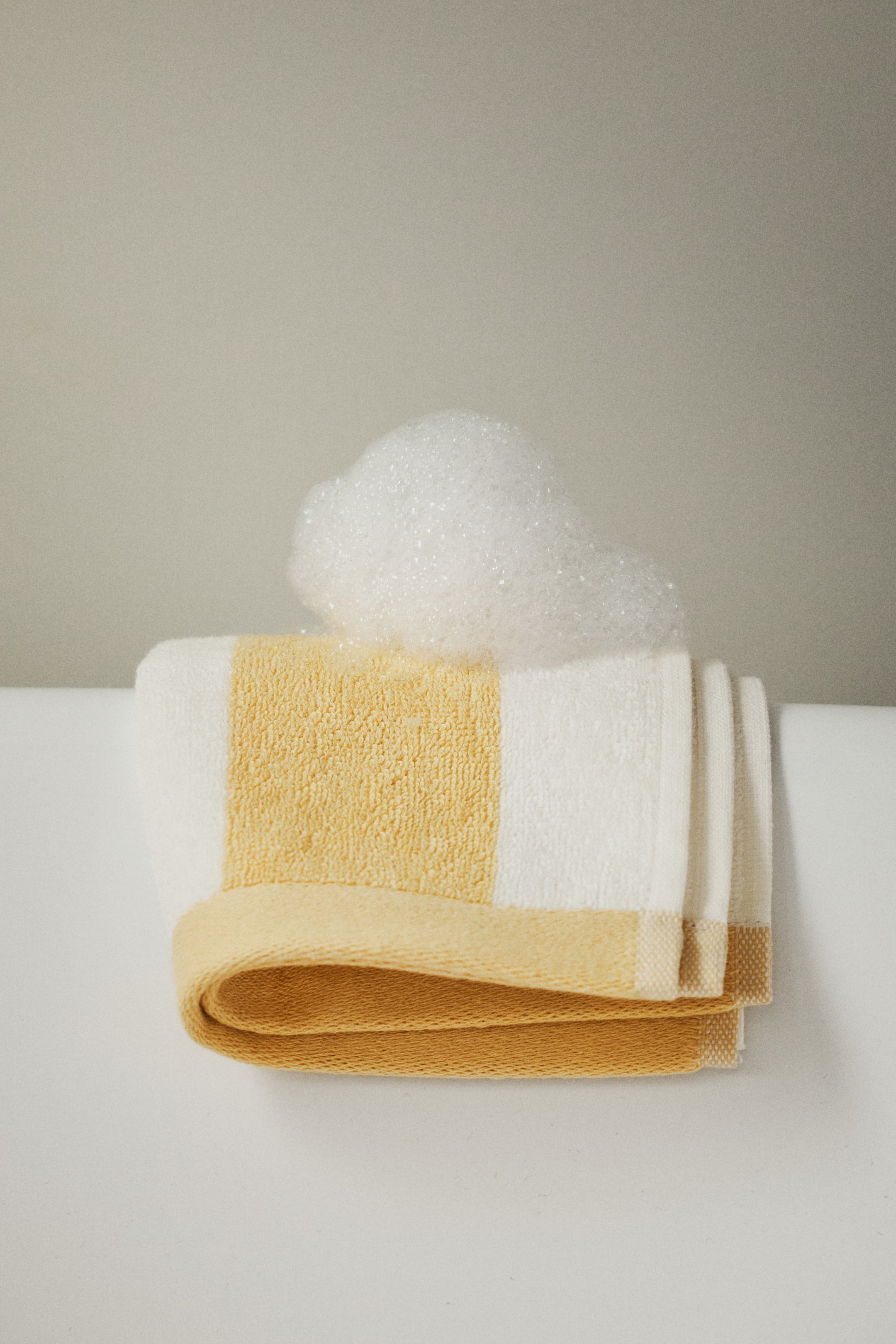 Ampliar la imagen: Una toalla de invitados doblada presenta su vista frontal, con un patrón de rayas de felpa de algodón blanco y amarillo.