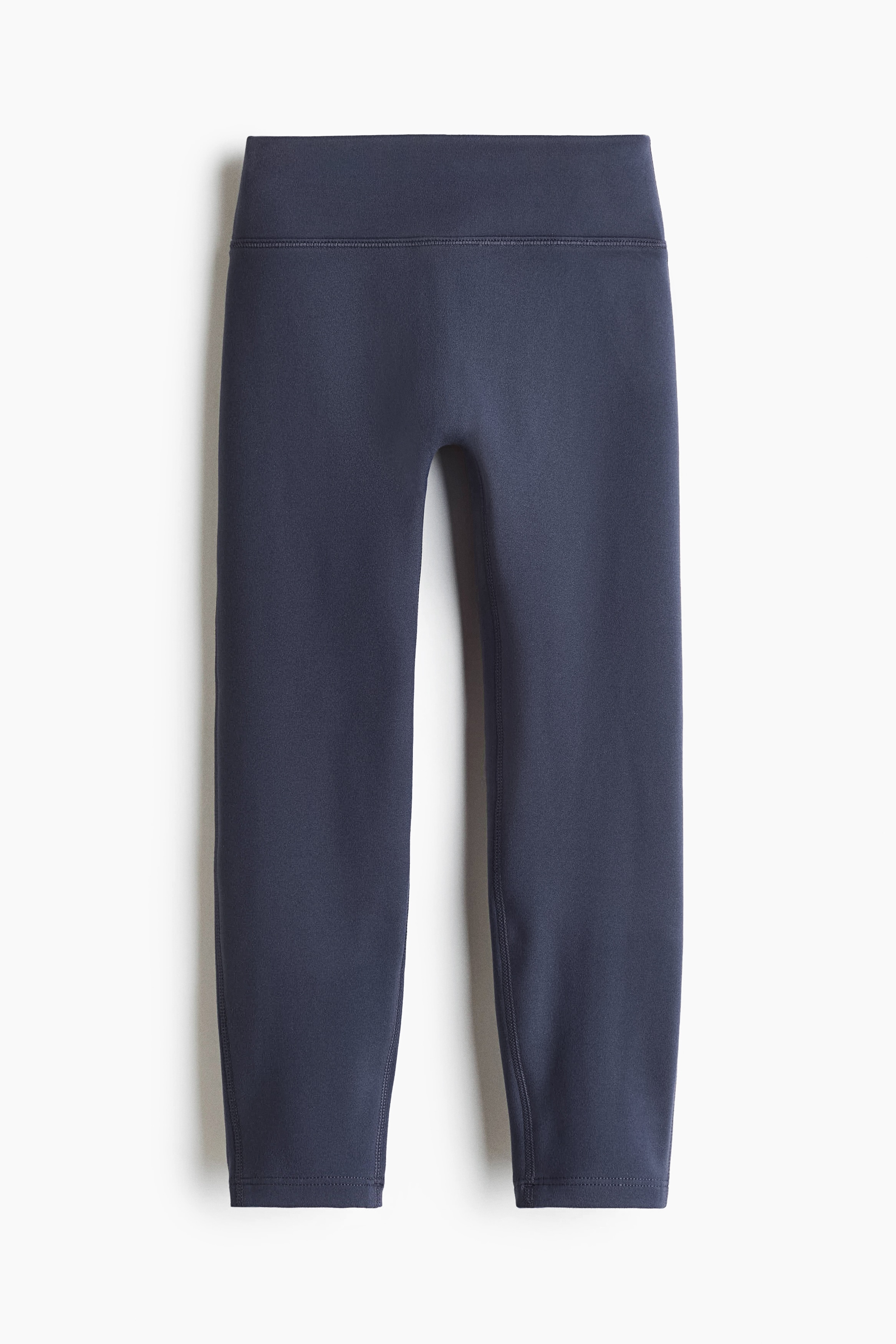 De donker marineblauwe bijpassende activewearset, van voren getoond, bestaat uit een nauwsluitende top met ronde hals en lange mouwen, raglanmouwen en boorden aan de mouwen, gecombineerd met bijpassende leggings tot op enkelhoogte. De set wordt gedragen door een model dat recht naar voren kijkt, gestyled met witte sneakers.