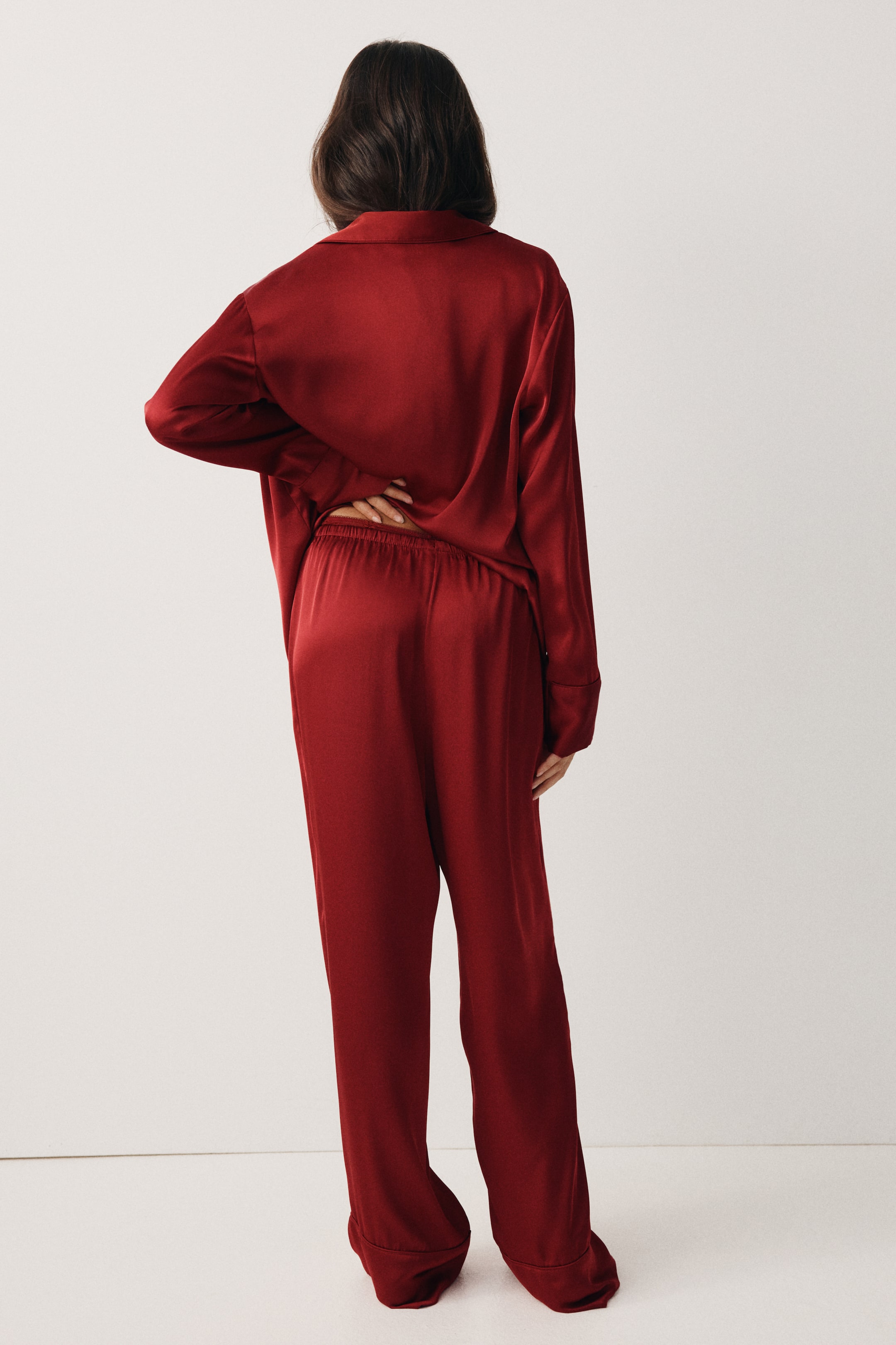 View larger image: A deep red two-piece set, crafted from a satin-like fabric, is being shown from the back. The loose-fitting long-sleeved top is featuring a collar, and the coordinating pants are presenting an elastic waistband at the back with a relaxed, straight-leg cut.