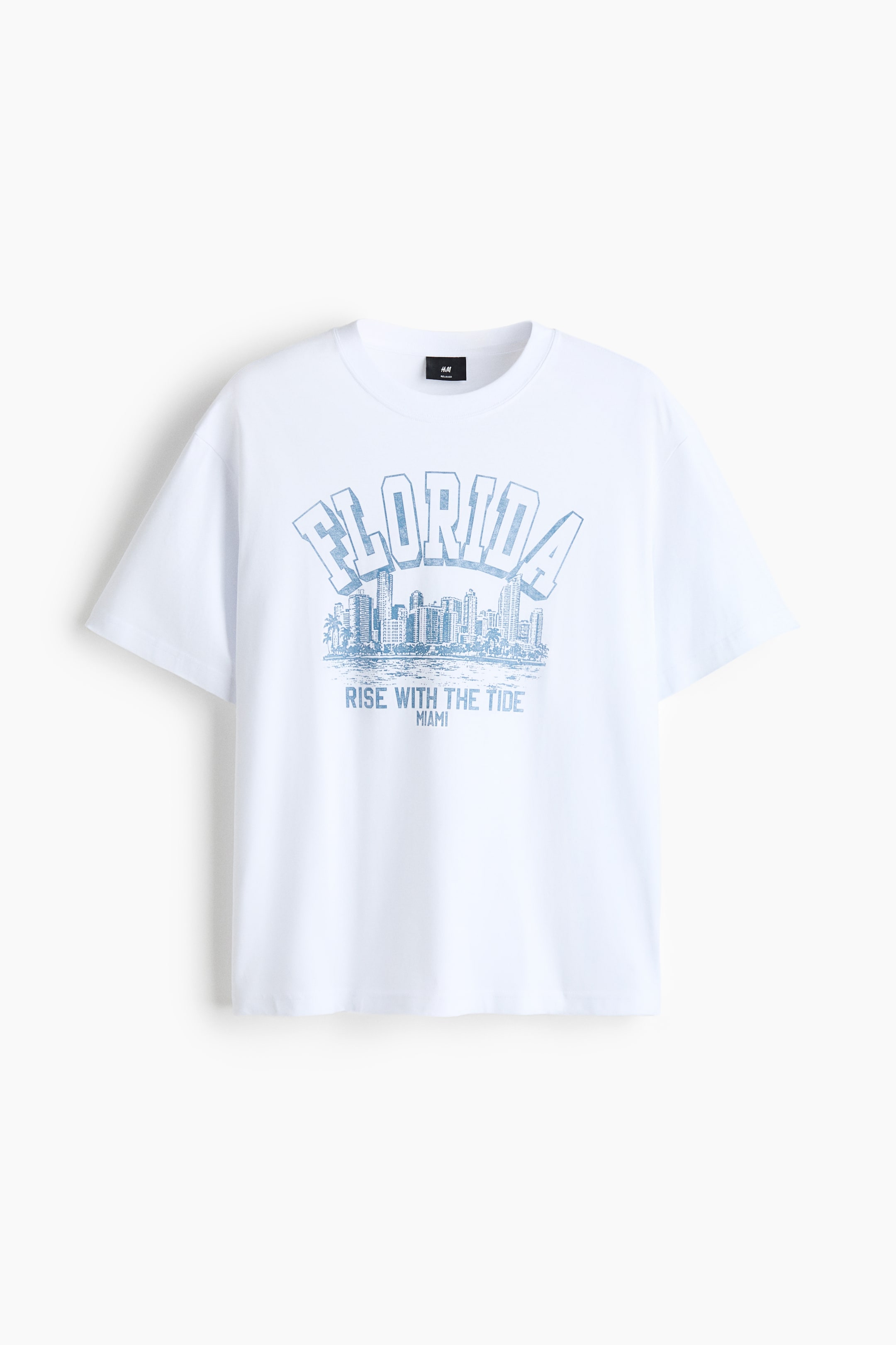 Ver imagen más grande: La camiseta blanca se muestra desde el frente, con un estampado gráfico desgastado en azul claro de la palabra arqueada "FLORIDA" sobre una ilustración del paisaje urbano, con "RISE WITH THE TIDE MIAMI" impreso debajo. Está diseñada con un cuello redondo con ribete, hombros caídos y un dobladillo recto, presentando un ajuste holgado.