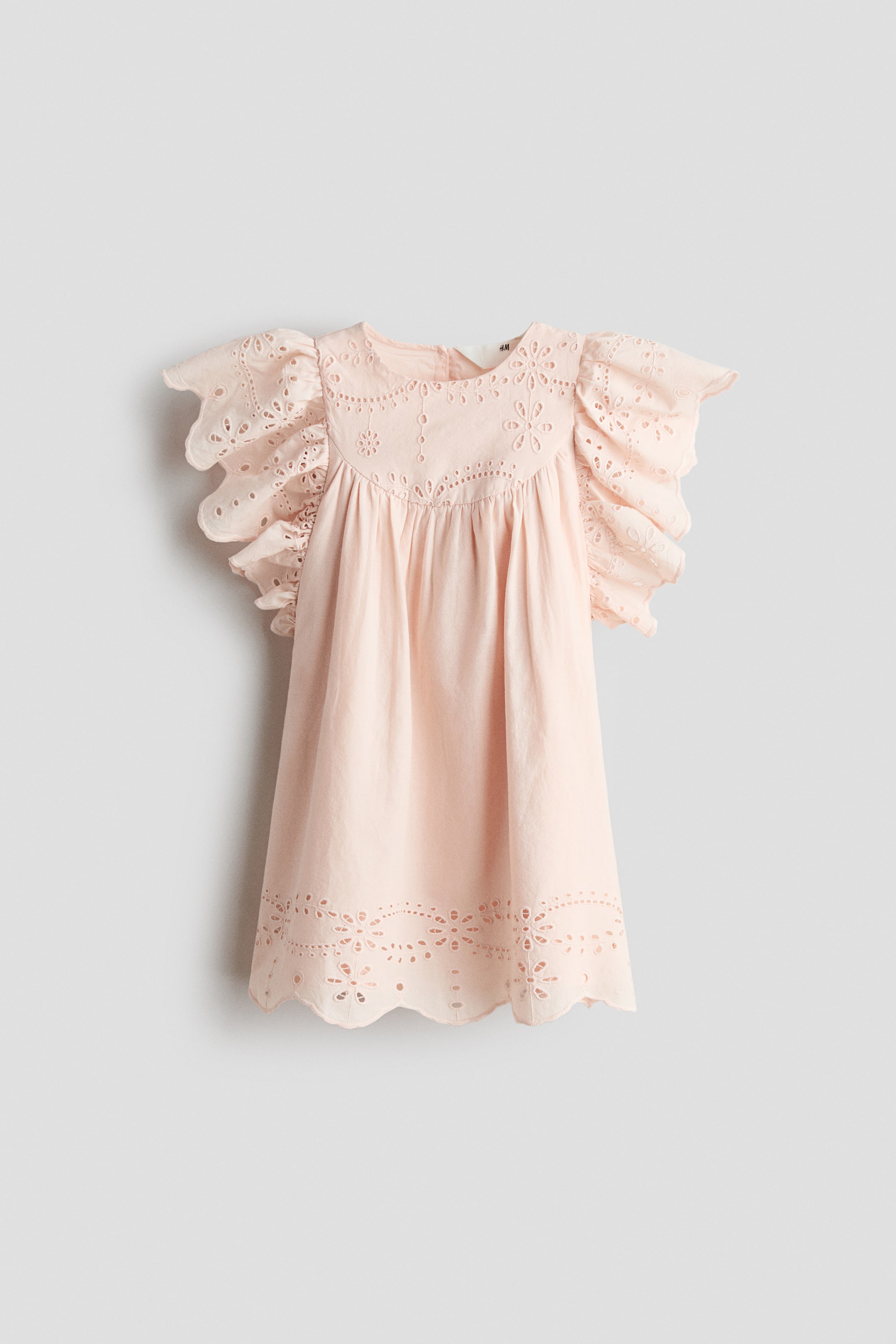 View larger image: A pink A-line dress in a light cotton weave is showcased from the front, featuring a round neckline and a yoke with a gathered seam. Broderie anglaise detailing enhances the neckline, yoke, scalloped butterfly sleeves, and scalloped hem.