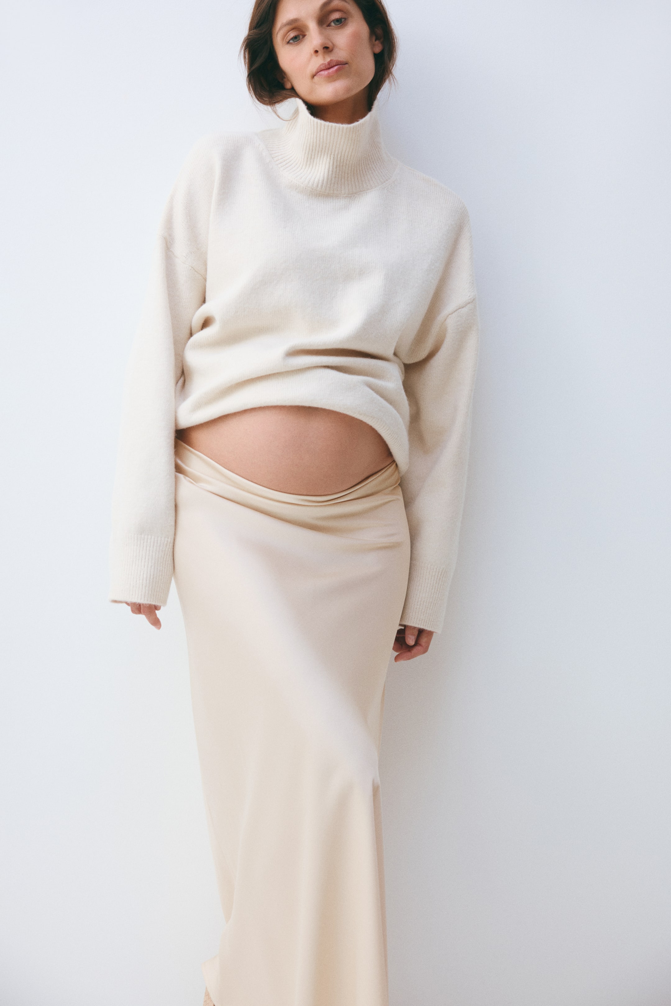 View larger image: A light beige turtleneck sweater is worn, featuring a ribbed turtleneck and ribbed cuffs. Its relaxed hem rests above the waist of a matching light beige flowing skirt, which sits low.