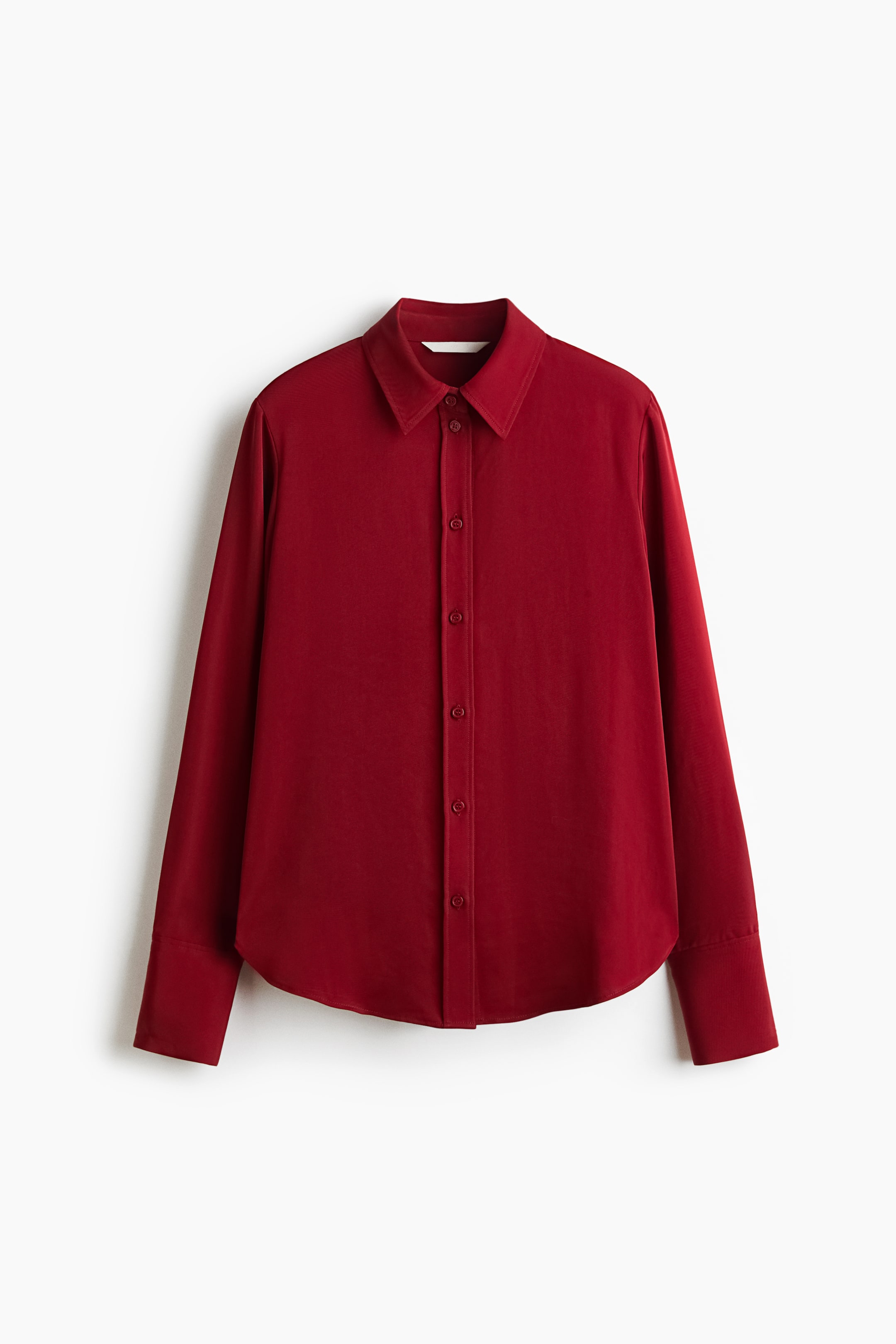 View larger image: A deep red long-sleeved button-down shirt is facing front, showcasing a pointed collar and a centre-front button placket with matching red buttons. The shirt features long sleeves with wide, structured cuffs and a gently curved hemline.