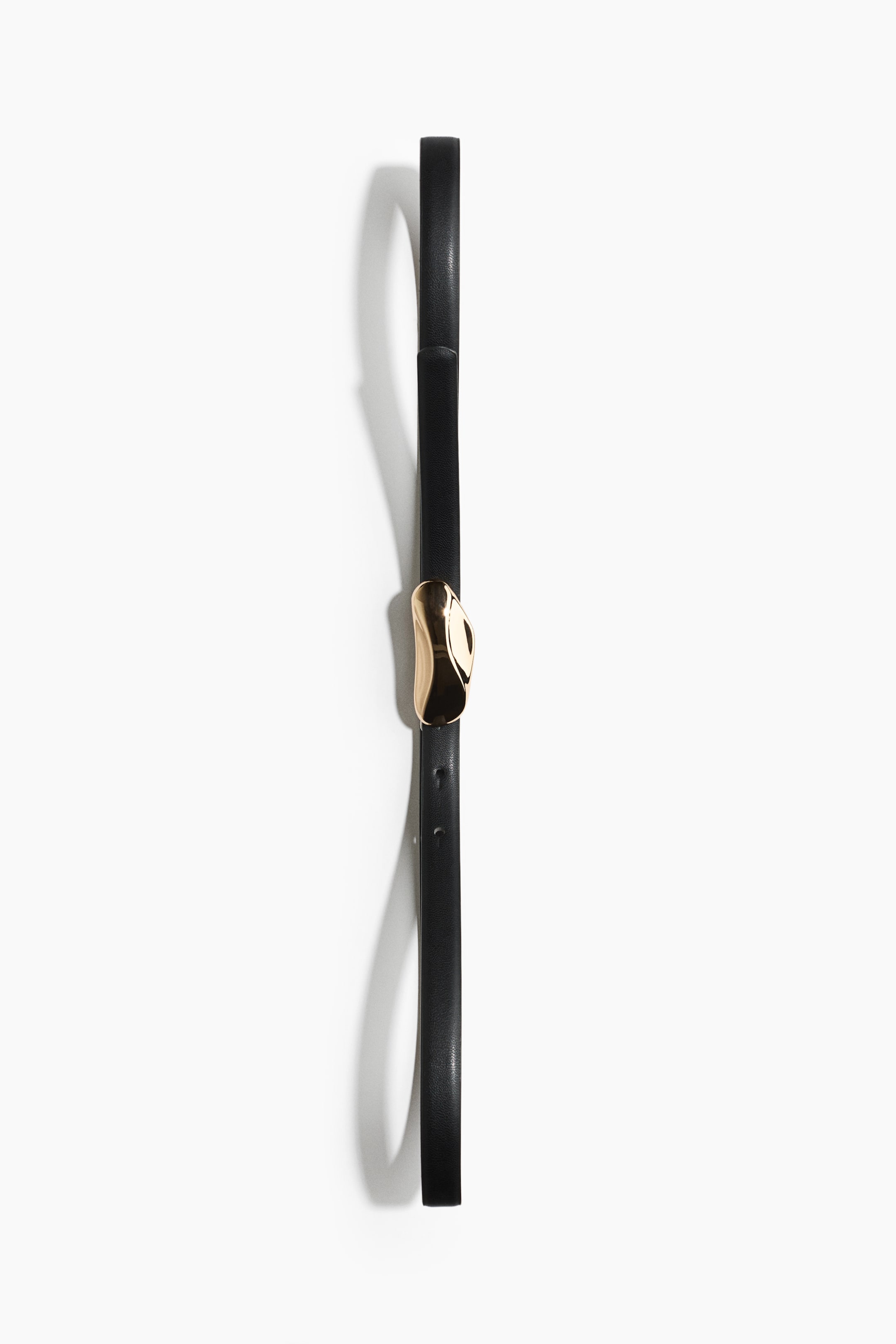 View larger image: A black coated fabric belt is shown front on, displayed vertically in a fastened loop. The belt features a shiny, gold-toned metal buckle with a sculptural, softly curved, asymmetrical shape.