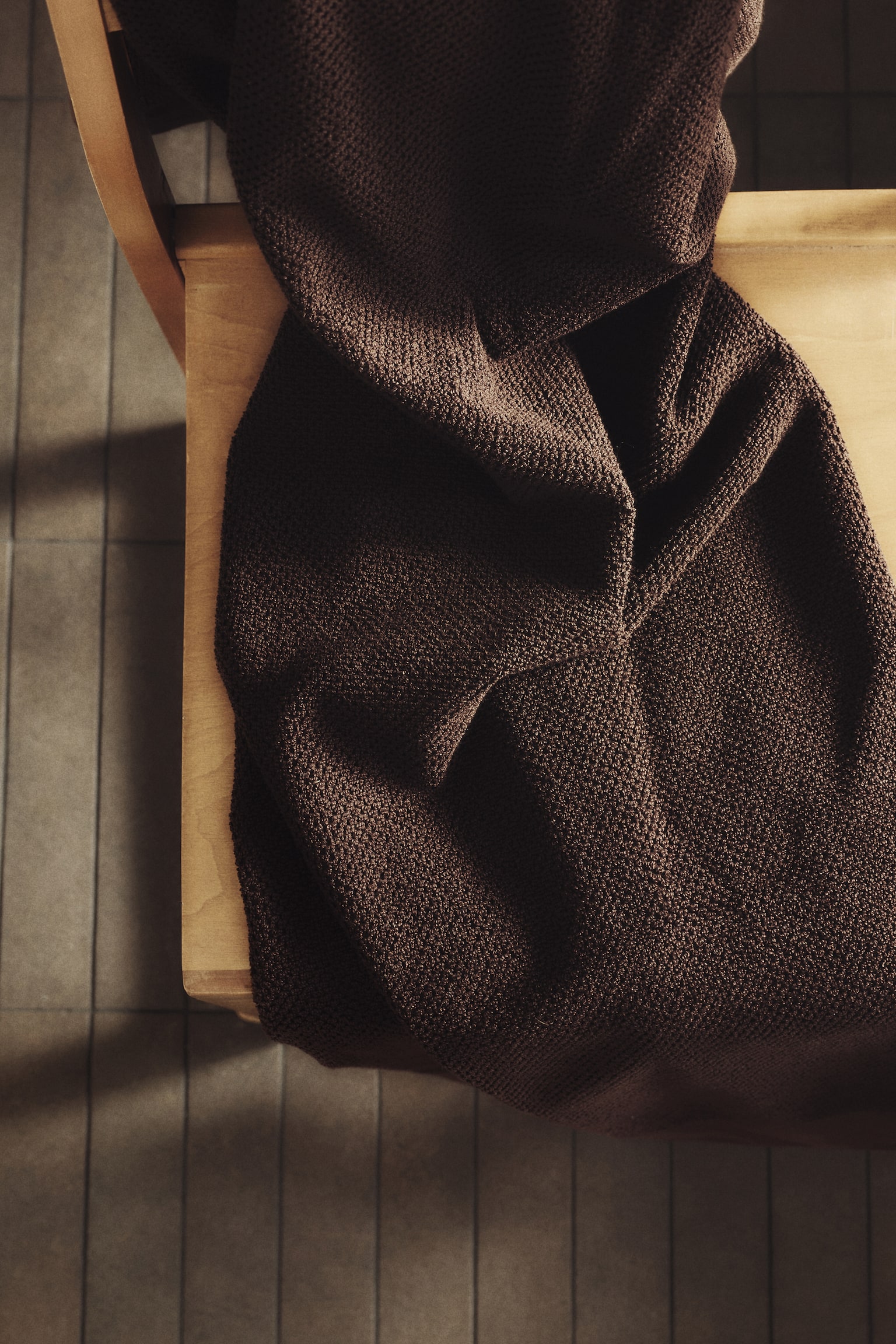 A dark brown bath towel is draped, showcasing its rich colour and a distinct, small, raised textured weave across its surface. - 1