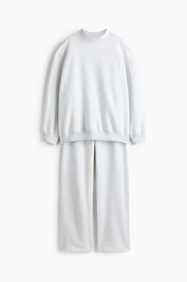 A matching light grey lounge set is shown from the front, featuring a long-sleeved sweater with a high ribbed neck, dropped shoulders, and ribbed finishes at the cuffs and hem. The matching straight-leg track pants are draped below, completing the relaxed-fit two-piece outfit. - 1