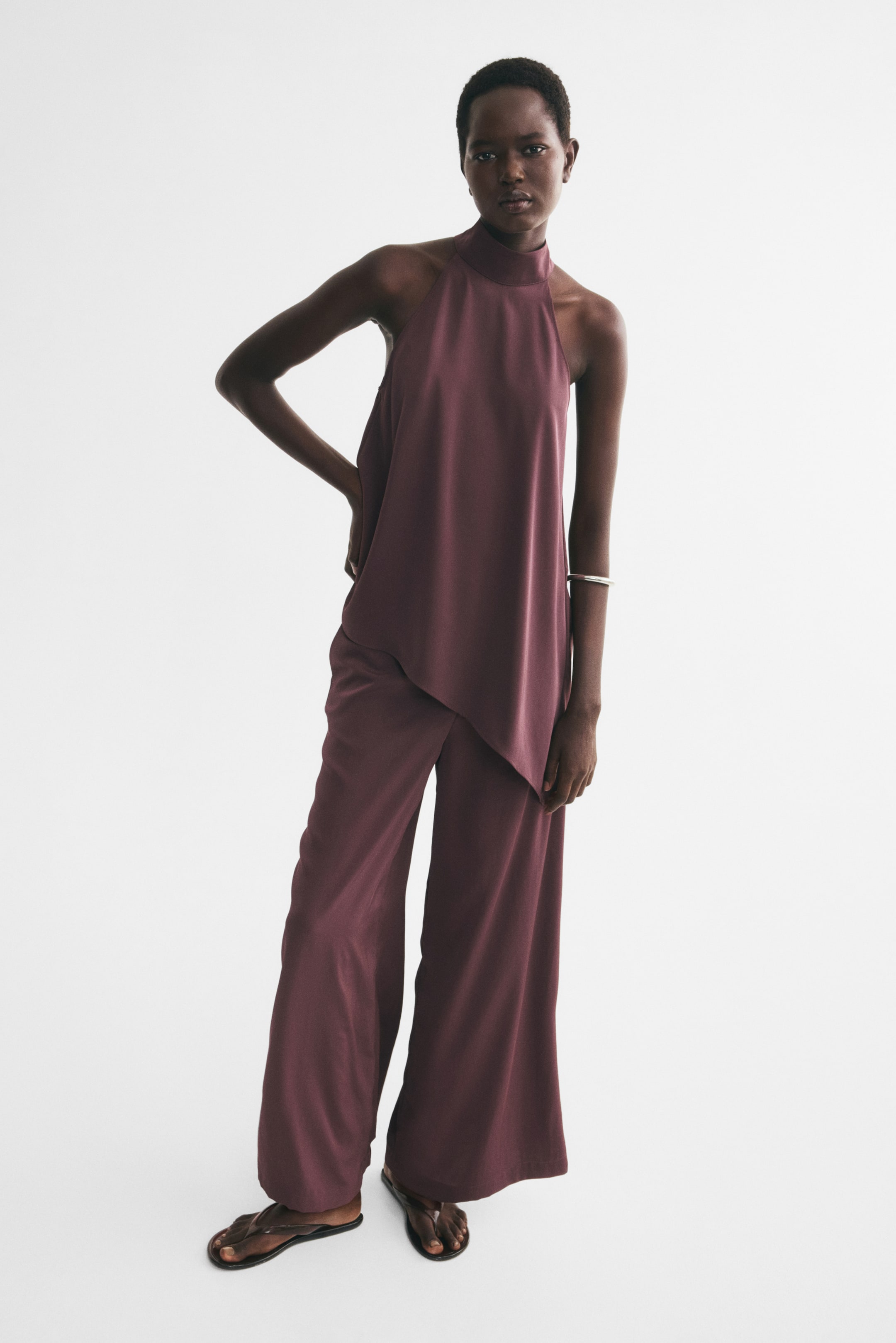 View larger image: Wide-leg pants in a dark plum woven fabric with a slight sheen are being worn by the model, paired with a matching sleeveless halter-neck top. The pants feature a relaxed fit and drape loosely to the feet, where they are styled with flat sandals.