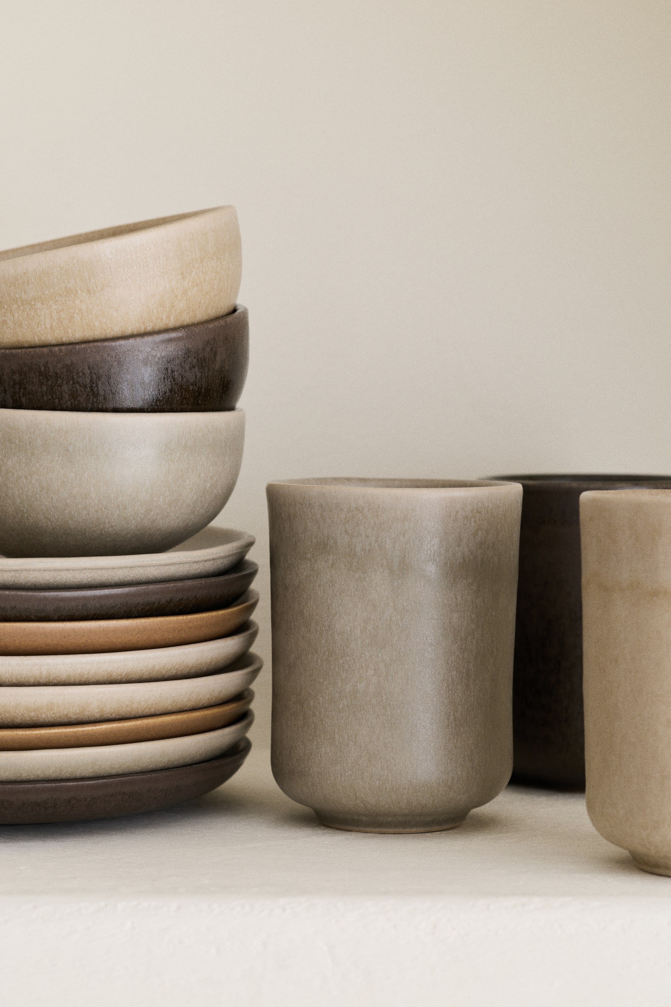 Agrandir l'image: Trois tasses en grès sont disposées debout, mettant en valeur divers émaux et finitions texturées. La tasse à l'avant est de couleur taupe clair, avec une tasse marron foncé et une tasse beige plus claire partiellement visibles derrière elle.