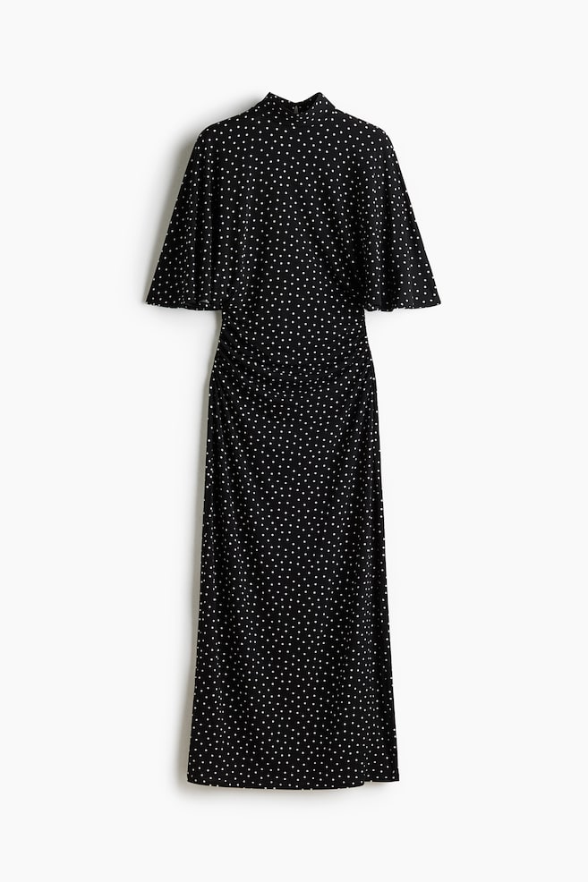 A long black jersey dress with white polka dots is shown from the front, featuring a stand collar and elbow-length butterfly sleeves. The dress has gathered side seams at the waist that drape into a straight-cut long skirt. - 1