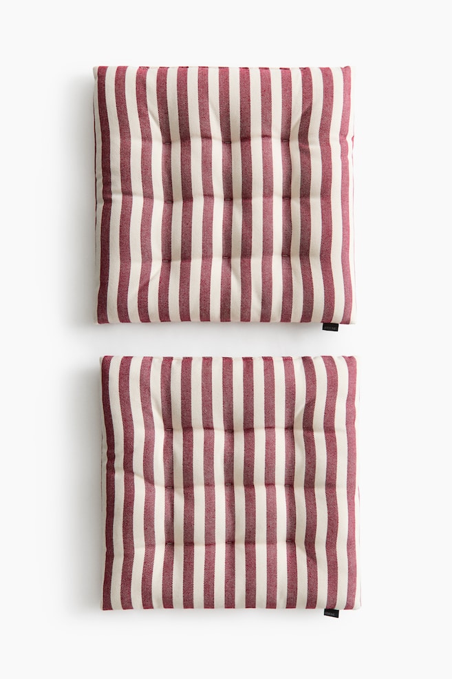 Two square padded seat cushions are shown from a front overhead view, featuring a vertical striped pattern in dark red and off-white. The cushions display evenly spaced tufted quilt knots across their surfaces to maintain their shape. - 1