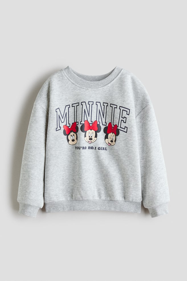 A light grey sweatshirt is lying flat, facing forward, featuring a round, rib-trimmed neckline, dropped shoulders, long sleeves, and ribbed cuffs and hem. The front is displaying a graphic print with "MINNIE" in outlined letters above three Minnie Mouse heads wearing red bows, and "YOU'RE NO.1 GIRL" printed below. - 1