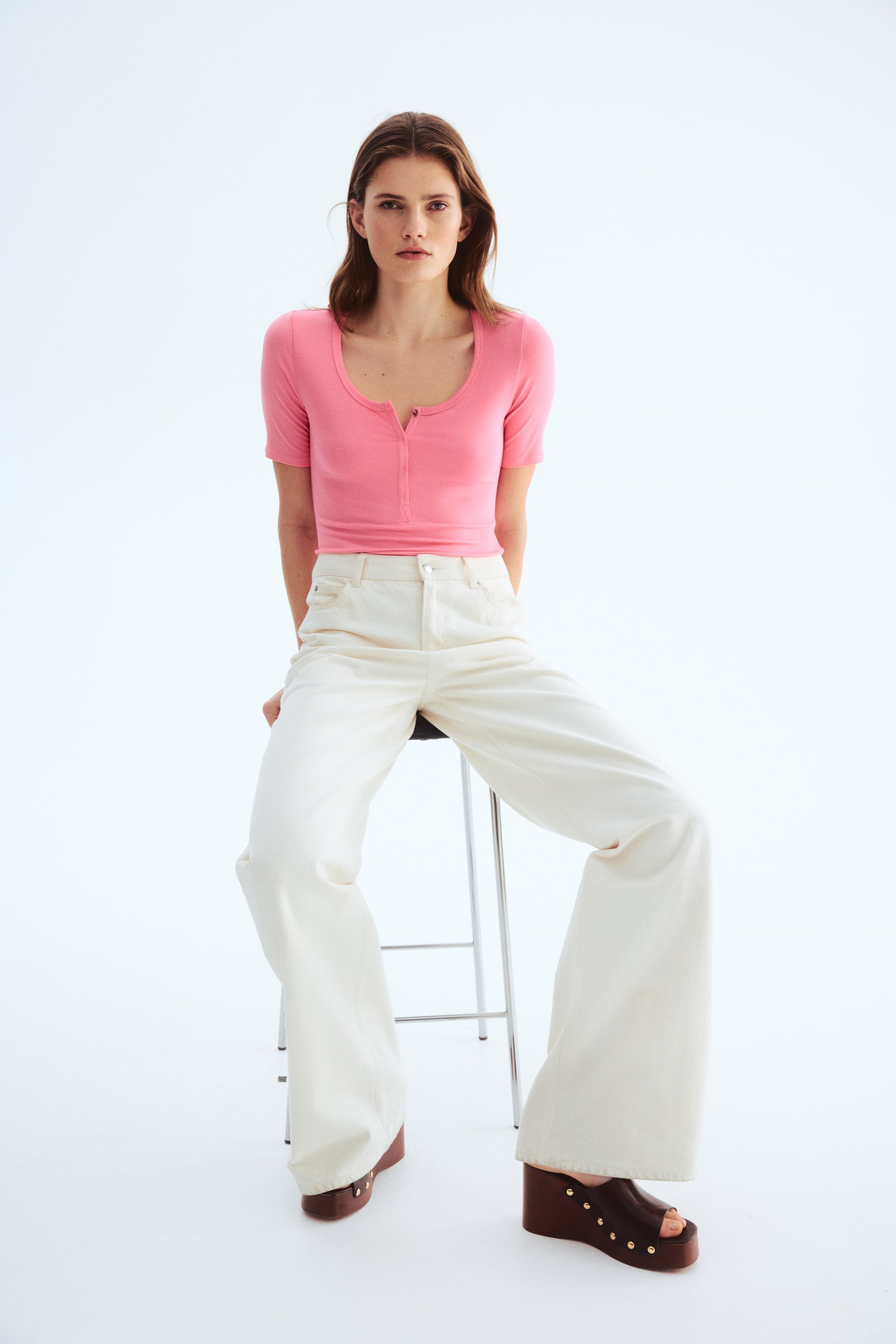 View larger image: Presenting a pink short-sleeved, finely ribbed knit top, which features a scoop neckline and a henley placket with buttons at the front. This fitted top showcases a cropped length, ending just above the waistband of light-coloured trousers.