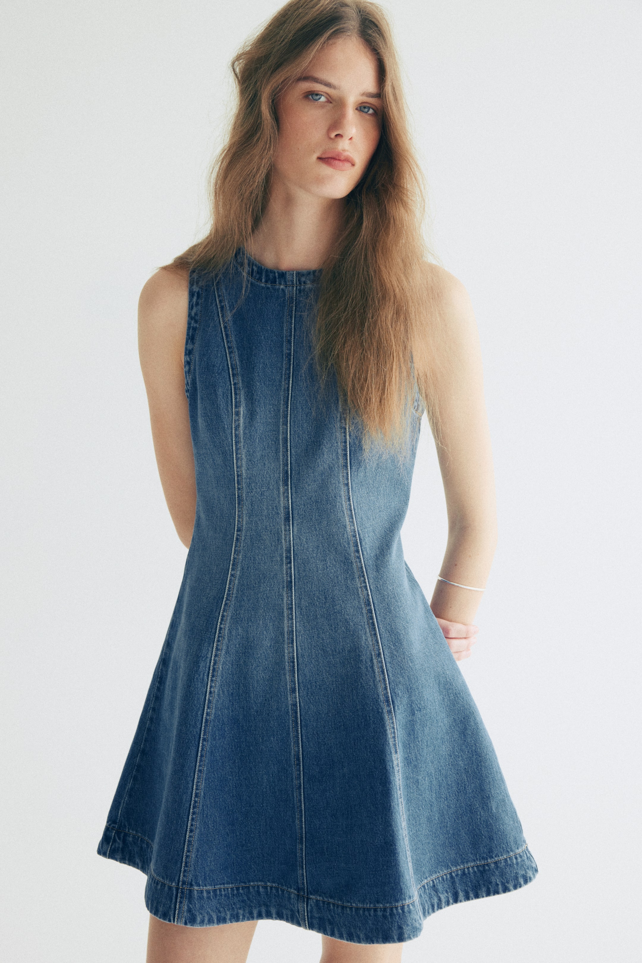 Größeres Bild anzeigen: Ein ärmelloses Kleid aus blauem Denim mit einem runden Halsausschnitt und vertikalen Nähten, die das Oberteil formen und in einen A-Linien-Rock auslaufen.