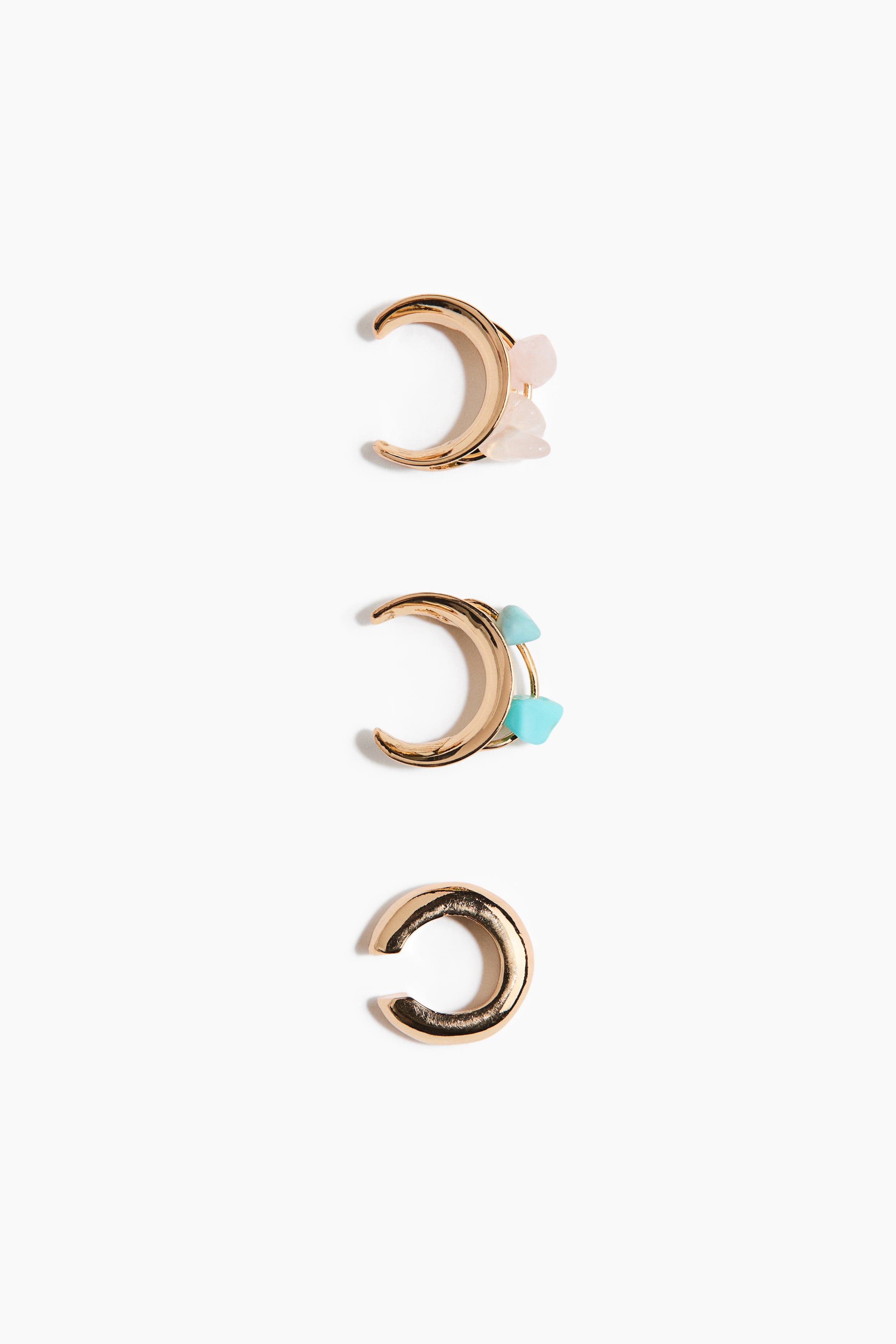 Agrandir l'image: Un ensemble de trois manchettes d'oreilles dorées est présenté, chacune arborant un design en forme de C. La manchette supérieure est ornée de plusieurs pierres roses aux formes irrégulières, tandis que la manchette du milieu présente des pierres de couleur bleu-vert aux formes similaires. La manchette inférieure affiche une finition dorée polie et épurée.