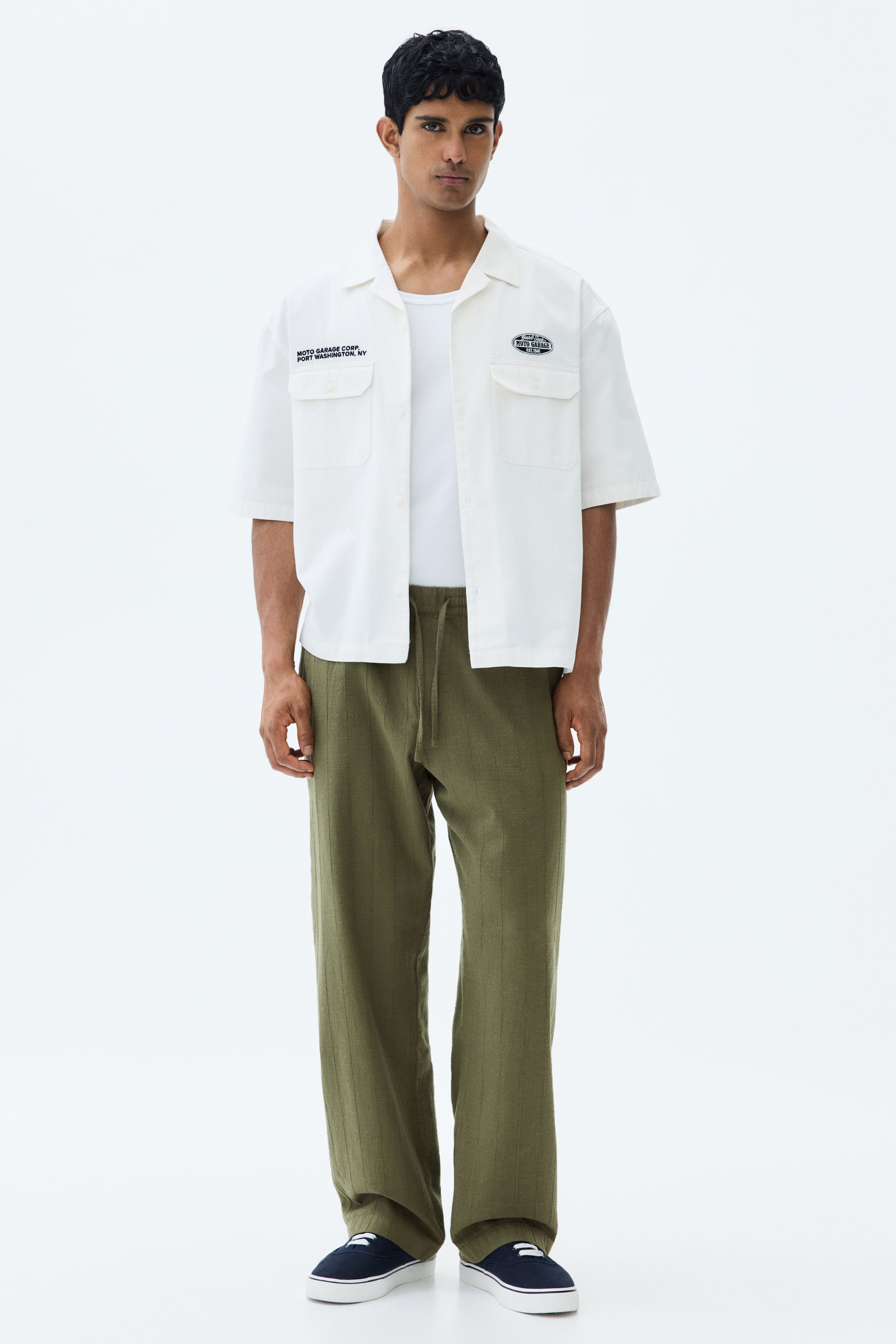 View larger image: The model is wearing trousers in an olive green hue, featuring a subtle vertical stripe texture and a drawstring at the waist, complete with side pockets and a relaxed fit.
