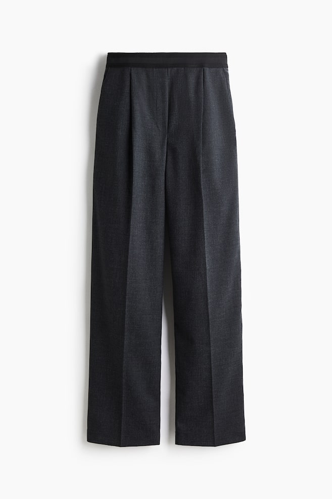 A pair of dark gray pants is shown from the front, featuring a flat black waistband, single front pleats, and straight legs with a prominent center crease. - 1