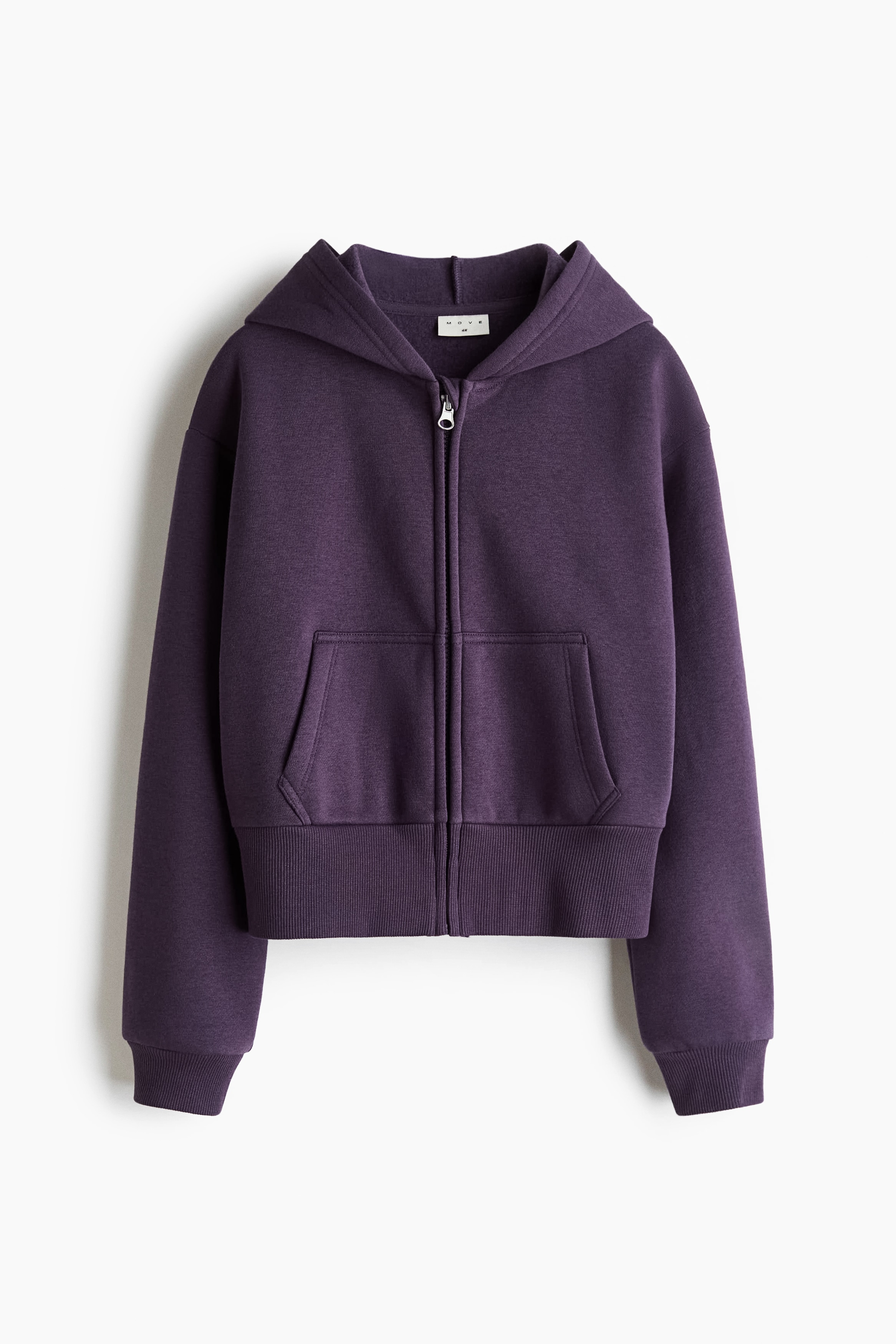 A dark purple zip-up hoodie is shown from the front, featuring a central zipper closure, dropped shoulders, long sleeves with ribbed cuffs, and split front pockets. The hoodie is being layered over a white t-shirt and paired with matching dark purple sweatpants.