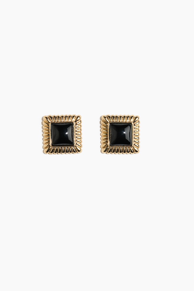 A pair of square stud earrings is facing front, showcasing a glossy, square black center stone surrounded by a textured, gold-toned ribbed border. - 1