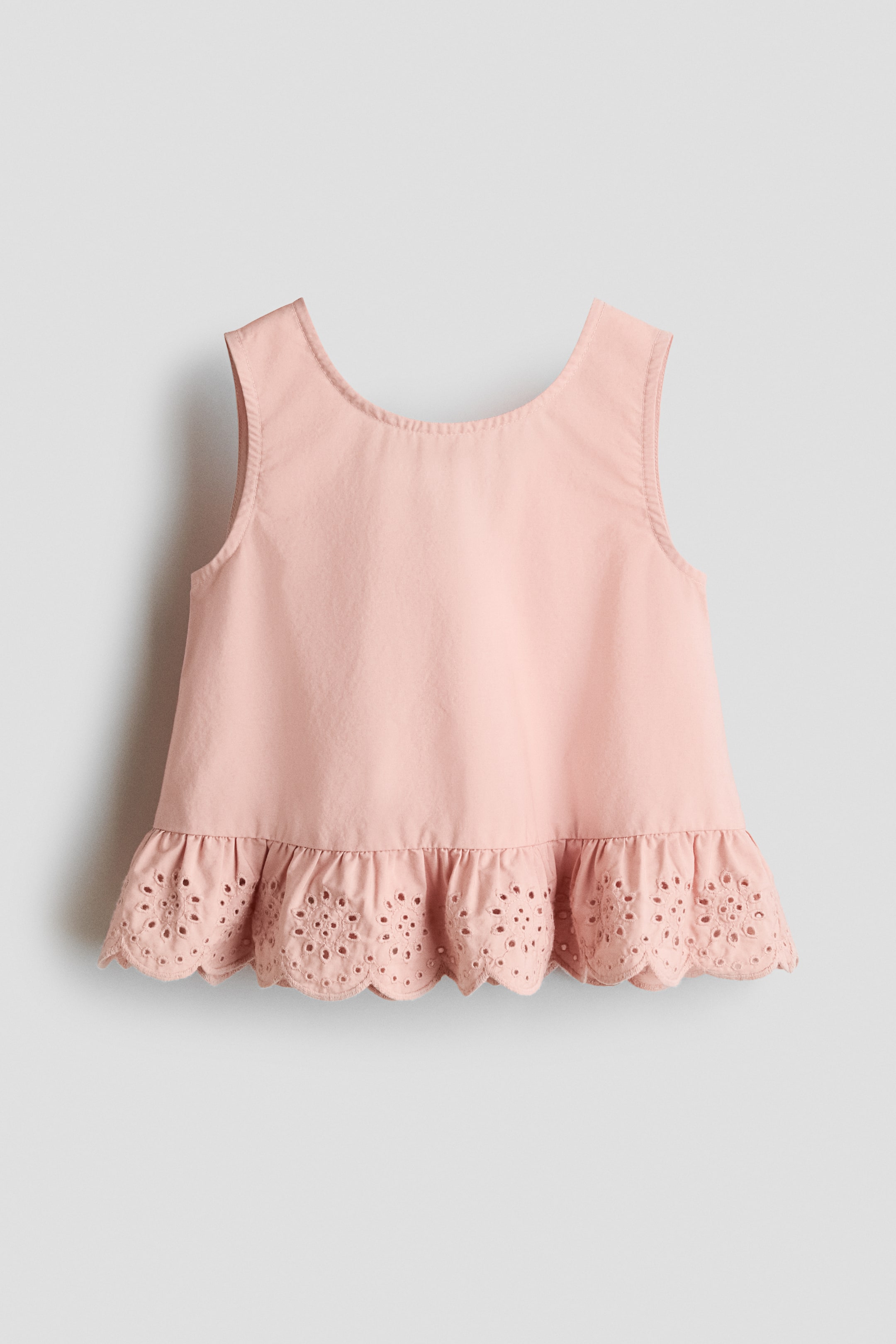 View larger image: A pink sleeveless top features a scoop neckline and a flared silhouette. Its hem has a ruffled design with eyelet embroidery and a scalloped edge.