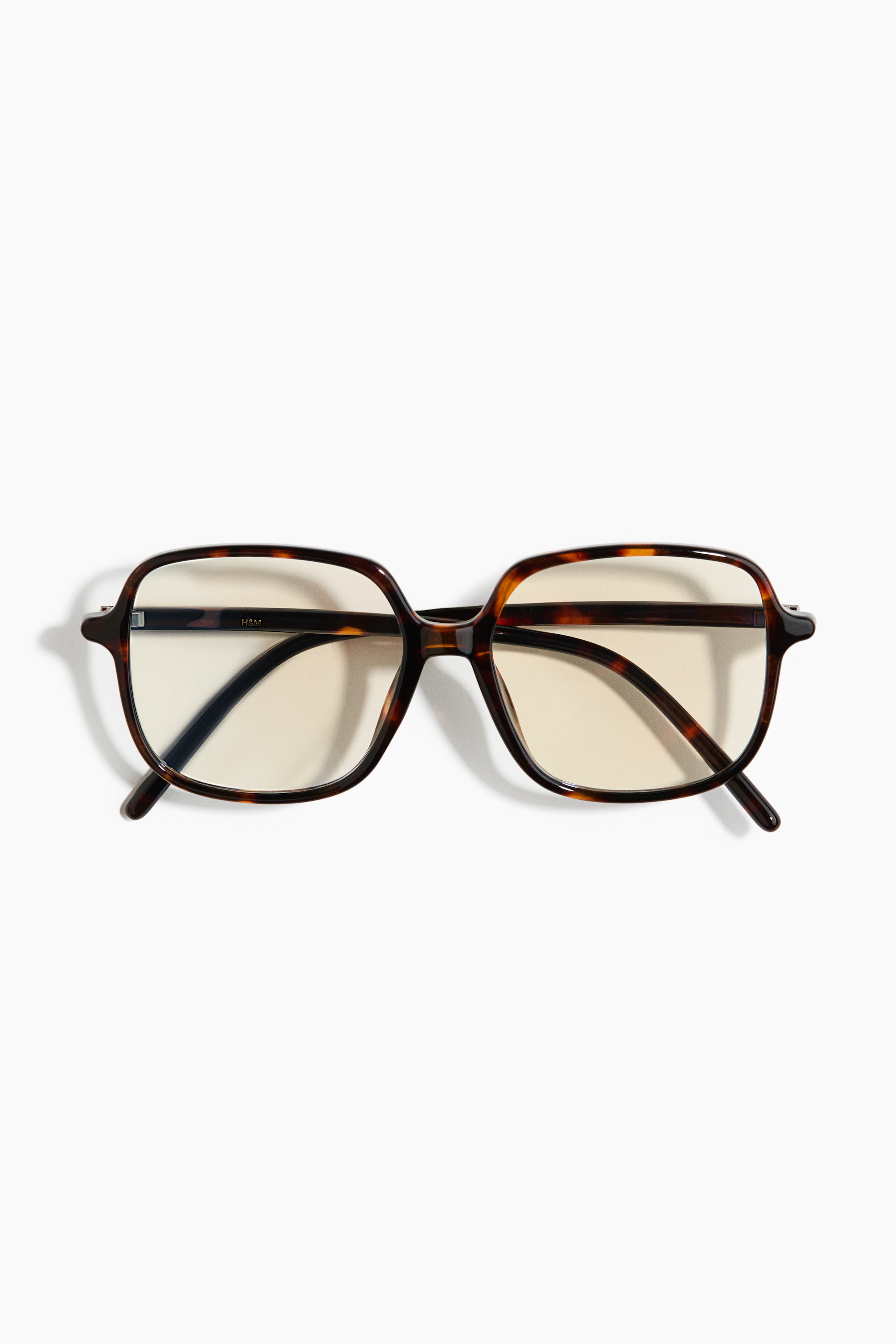 View larger image: A pair of glasses is shown from the front, featuring an oversized tortoiseshell frame with rounded rectangular lenses that have a slight yellow tint. Matching tortoiseshell temples extend outwards from the frame.