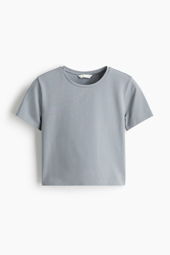 A short, fitted T-shirt in a muted blue-grey colour is being presented from the front, featuring a round neckline with a narrow trim and short sleeves. - 1