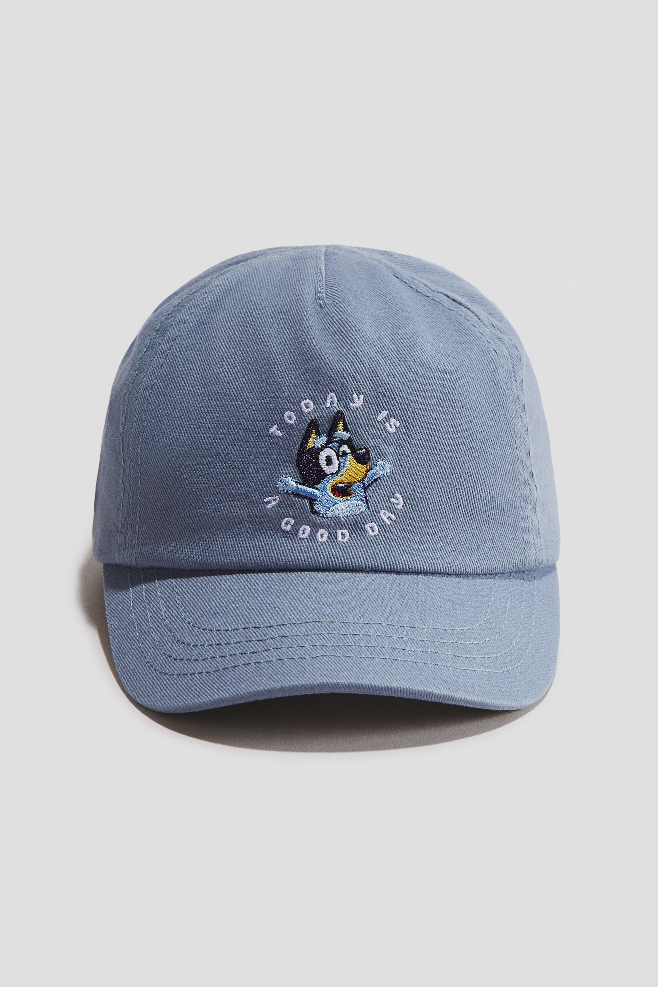 View larger image: A light blue cotton twill cap showcases its front, adorned with an embroidered blue dog character on the crown, accompanied by white text that reads 'TODAY IS A GOOD DAY' elegantly arching around it.