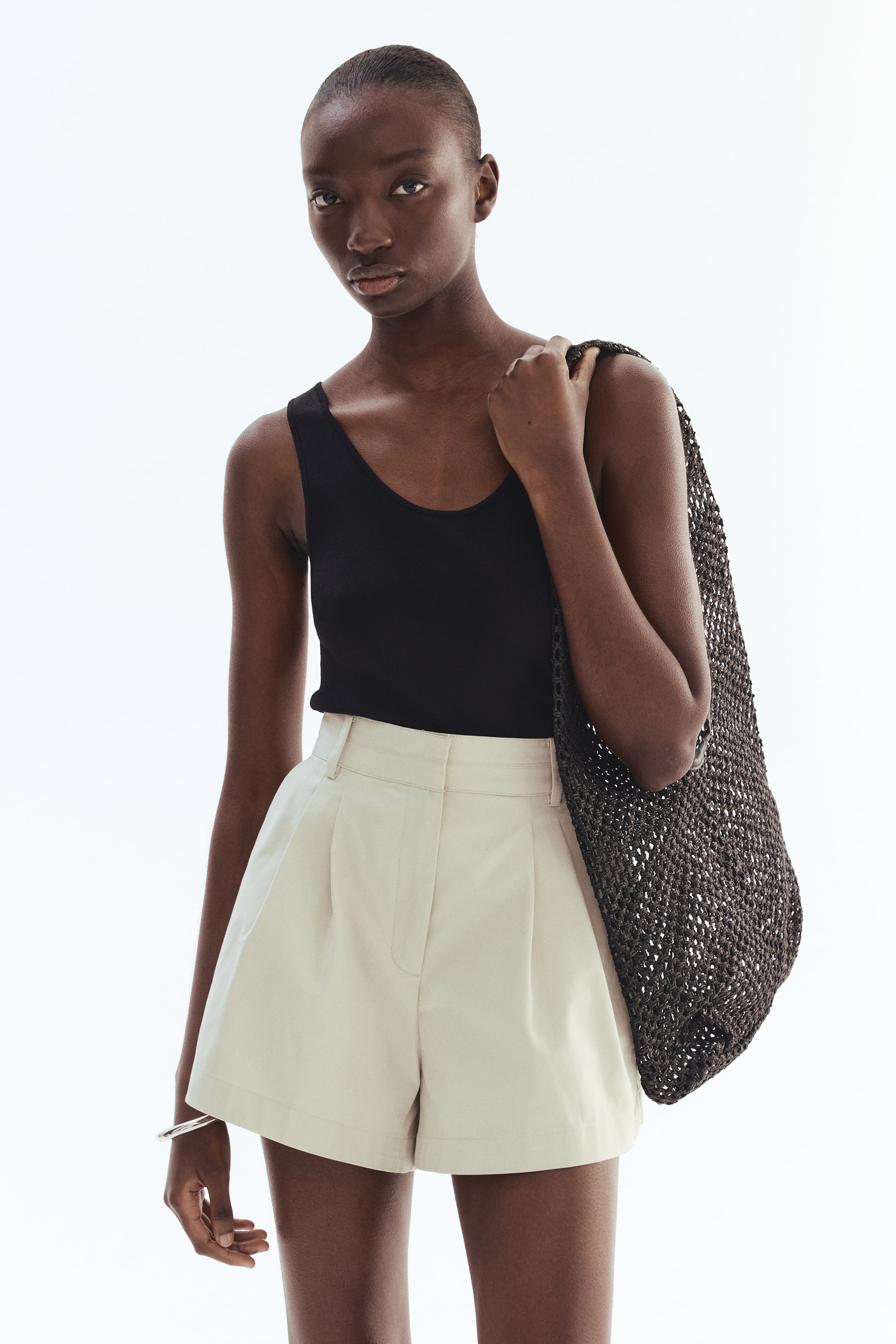 View larger image: A black ribbed tank top is being worn, featuring a scoop neck and wide shoulder straps. It is being presented tucked into light beige pleated shorts.