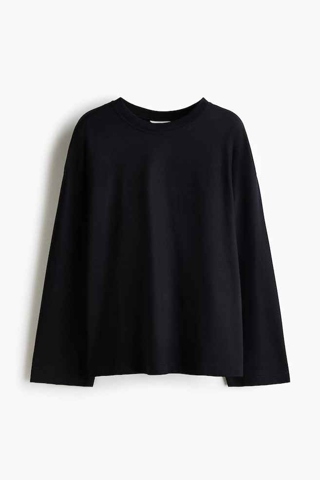 Ein schwarzes Langarm-T-Shirt hÃ¤ngt mit der Vorderseite nach vorn und zeigt eine lockere Passform mit Ã¼berschnittenen Schultern und einem klassischen Rundhalsausschnitt. Das KleidungsstÃ¼ck verfÃ¼gt Ã¼ber weit geschnittene, gerade Ãrmel und einen sauberen, geraden Saum. - 1
