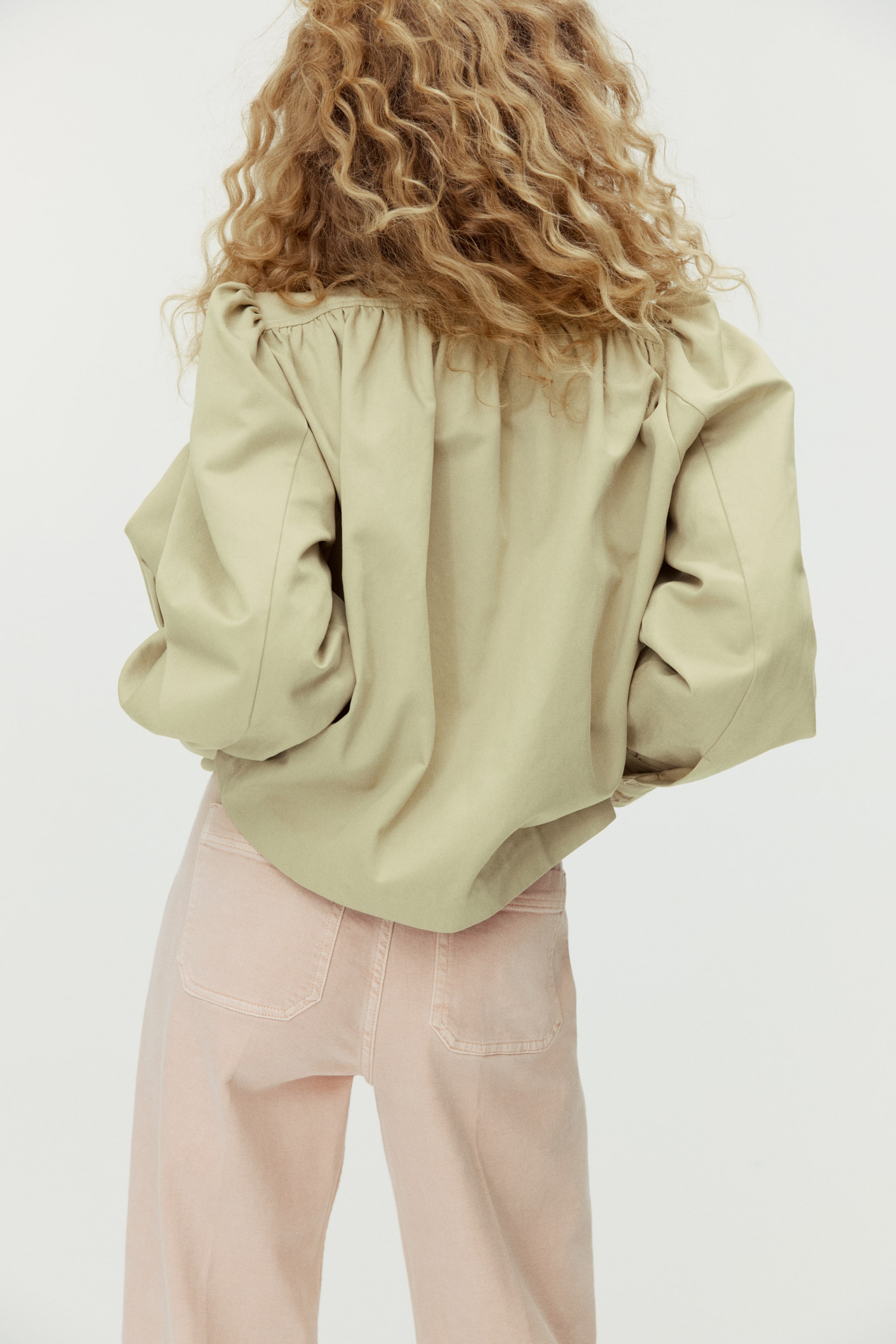 Voir une image plus grande: Une blouse volumineuse vert olive clair, avec des épaules froncées et des manches larges, est portée sur un pantalon rose pâle à jambes larges avec des poches arrière plaquées, le tout vu de dos.