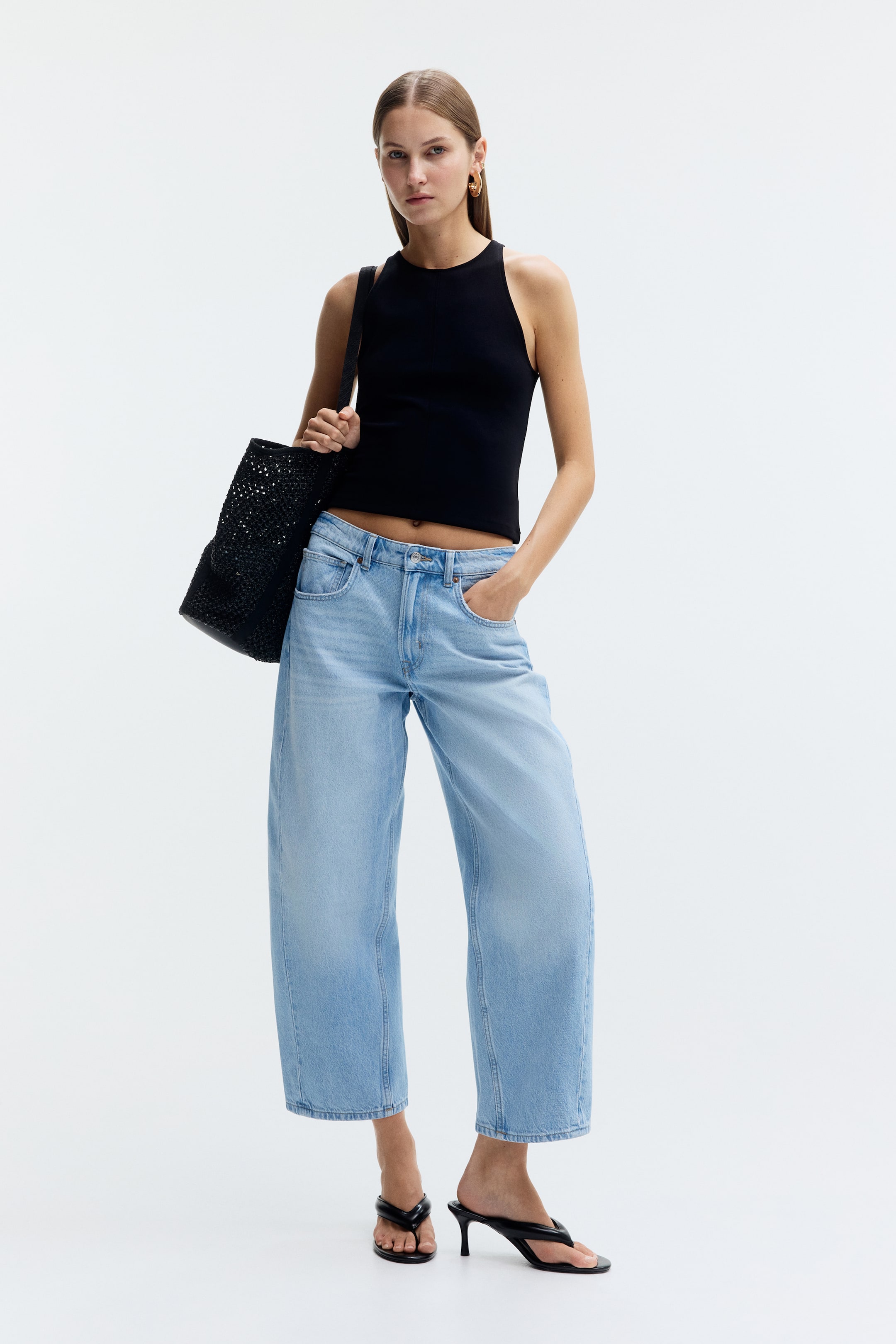 Grösseres Bild ansehen: Hellblaue 5-Pocket-Jeans aus Denim werden vom Modell getragen. Sie verfügen über eine normale Taille mit Knopf- und Reißverschluss sowie ein geschwungenes, voluminöses Bein, das zu einem knöchellangen Saum verjüngt. Das Modell steht mit einer Hand in einer der vorderen Taschen der Jeans, die mit schwarzen Sandaletten mit Absatz kombiniert sind.