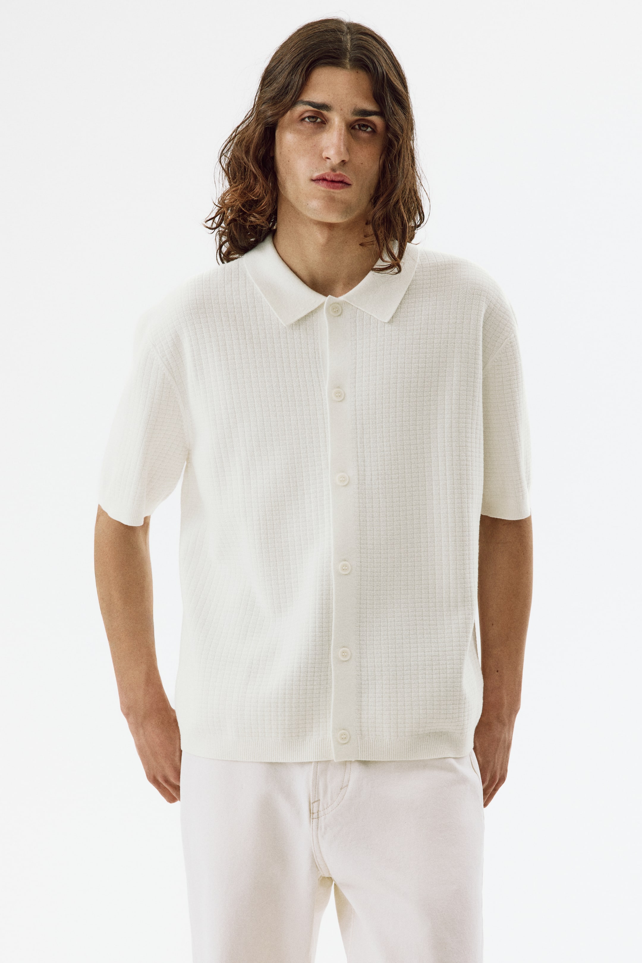 Voir une image plus grande: Un polo blanc à manches courtes en tricot est présenté de face, mettant en valeur une texture en maille gaufrée, un col polo classique, des manches courtes et une patte de boutonnage complète avec des boutons blancs. Il est fini avec un ourlet droit.