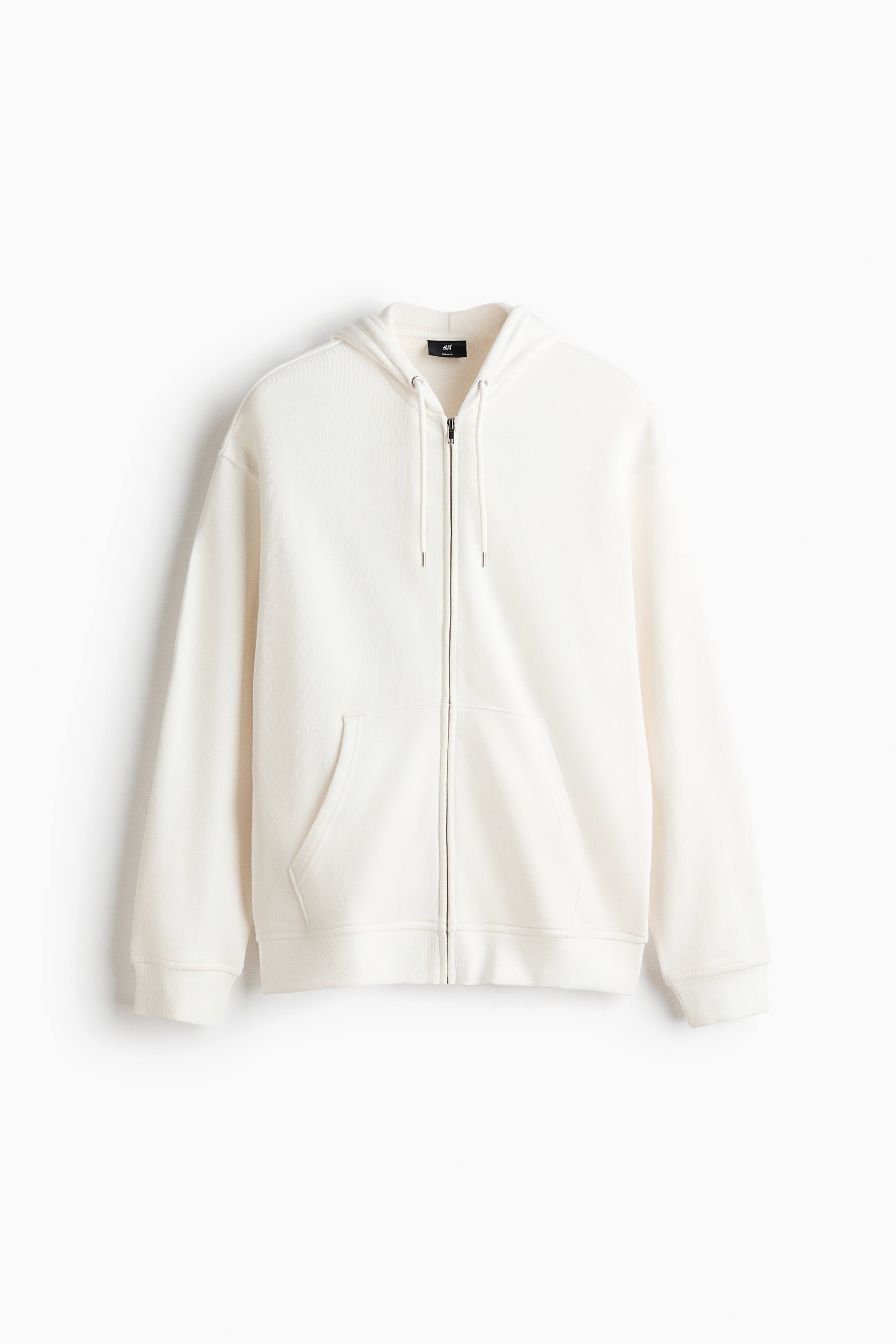View larger image: A cream zip-through hoodie in cotton sweatshirt fabric is shown from the front, featuring a hood with drawstrings, a front zipper, and front pockets. It is designed with dropped shoulders, long sleeves, ribbed cuffs, and a ribbed hem, showcasing a relaxed fit.