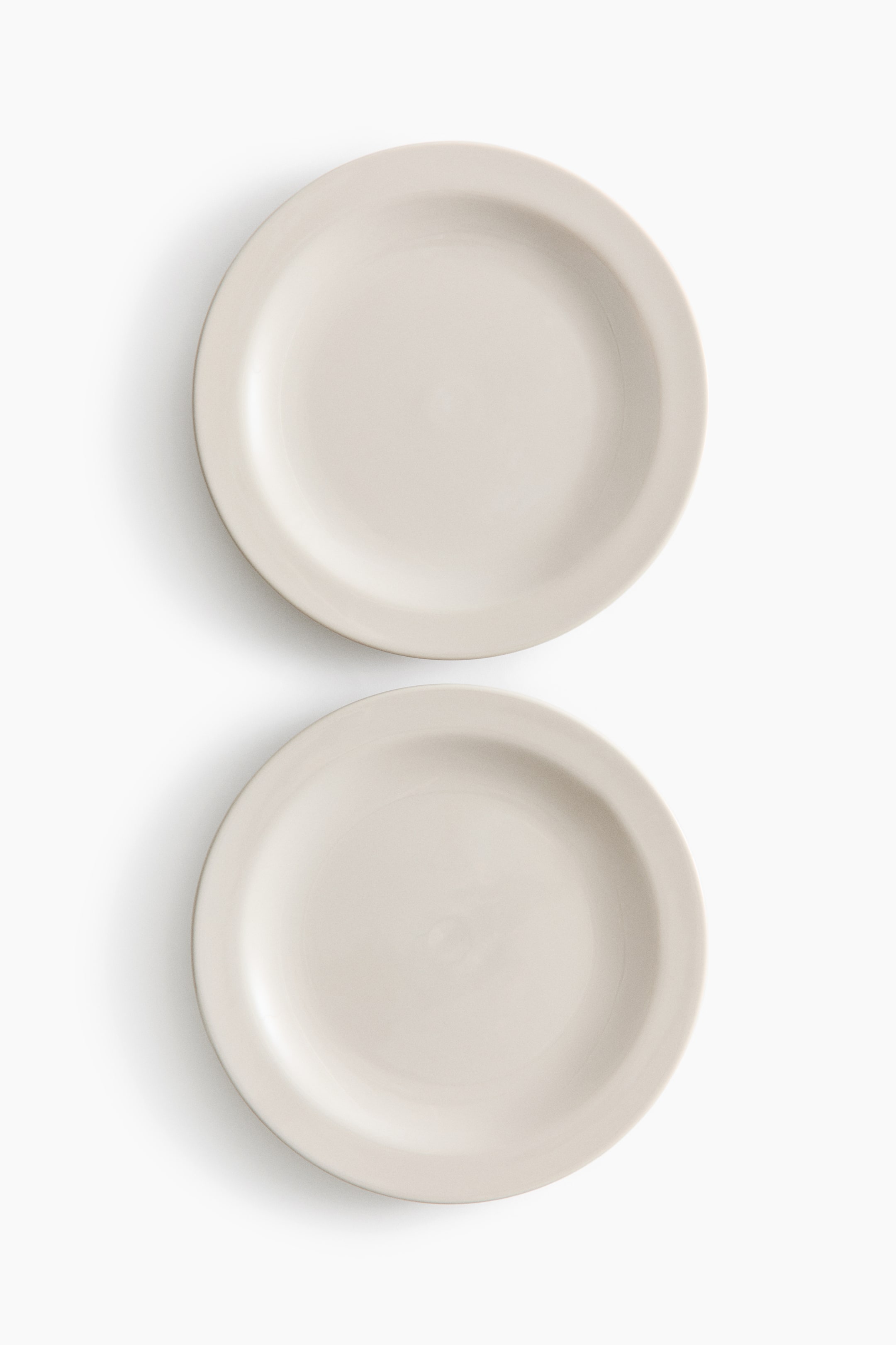 Agrandir l'image: Deux assiettes rondes de couleur beige clair sont disposées verticalement, l'une au-dessus de l'autre. Chaque assiette présente un centre plat et un rebord extérieur légèrement surélevé.