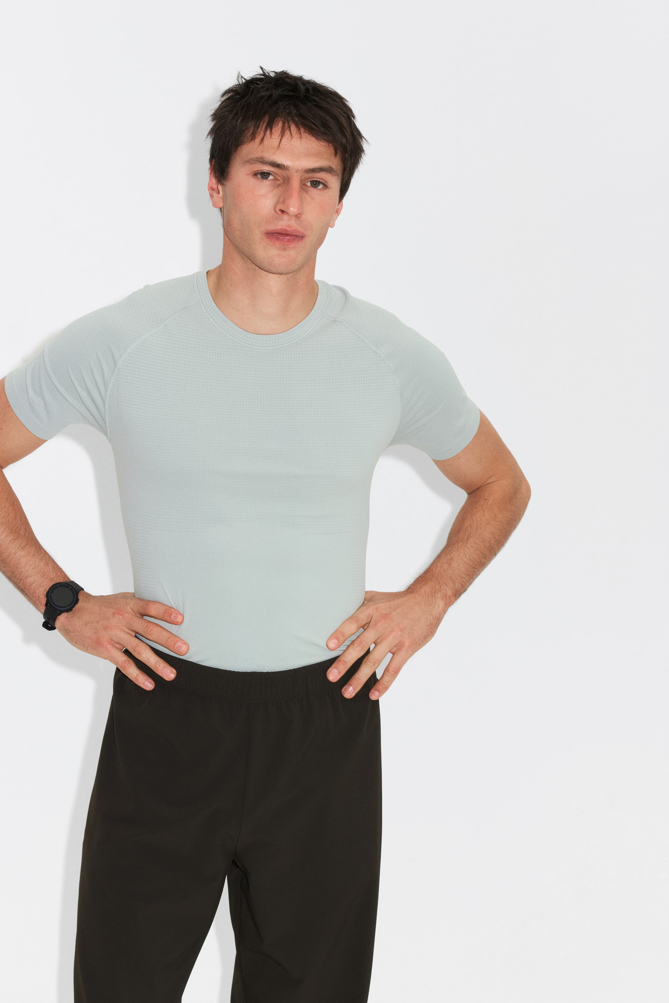 הצגת תמונה גדולה יותר: חולצת טי ספורטיבית בצבע אפור בהיר נלבשת, עם צווארון עגול ושרוולי רגלן קצרים. היא מציגה גזרה צמודה ומרקם עדין דמוי רשת על פני הבד.