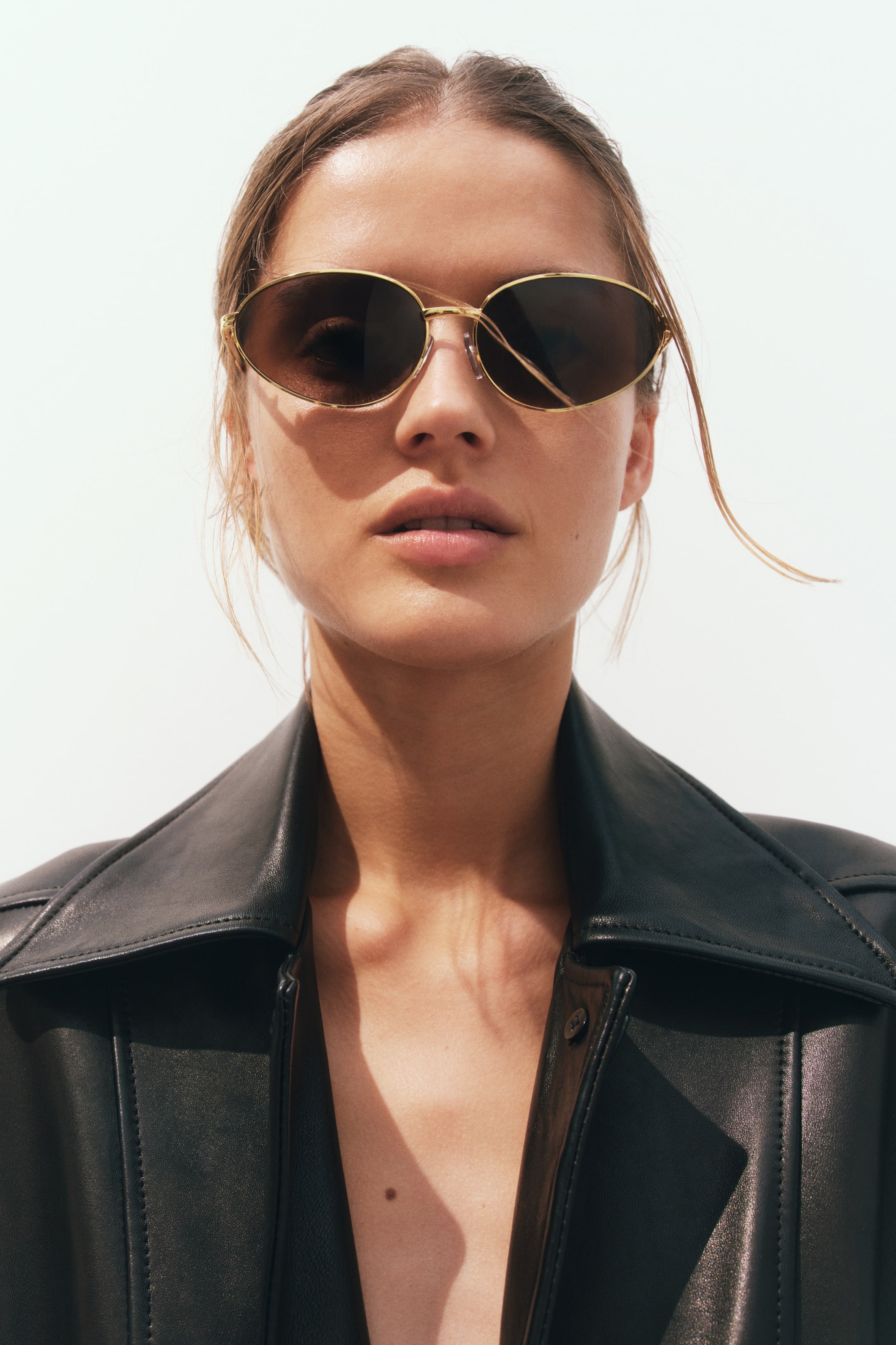 View larger image: The model is wearing oval sunglasses with metal sidepieces and adjustable nose pads, featuring tinted, UV-protective plastic lenses.