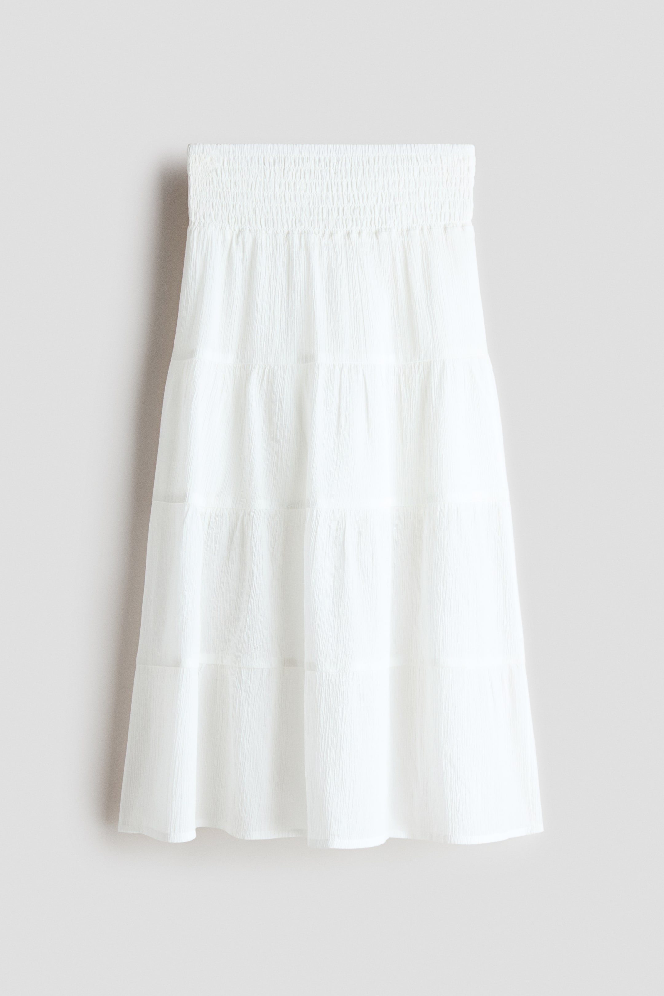 View larger image: The white skirt is shown from the FRONT, highlighting a shirred waistband and a tiered layout with multiple horizontal panels crafted from crinkled fabric.