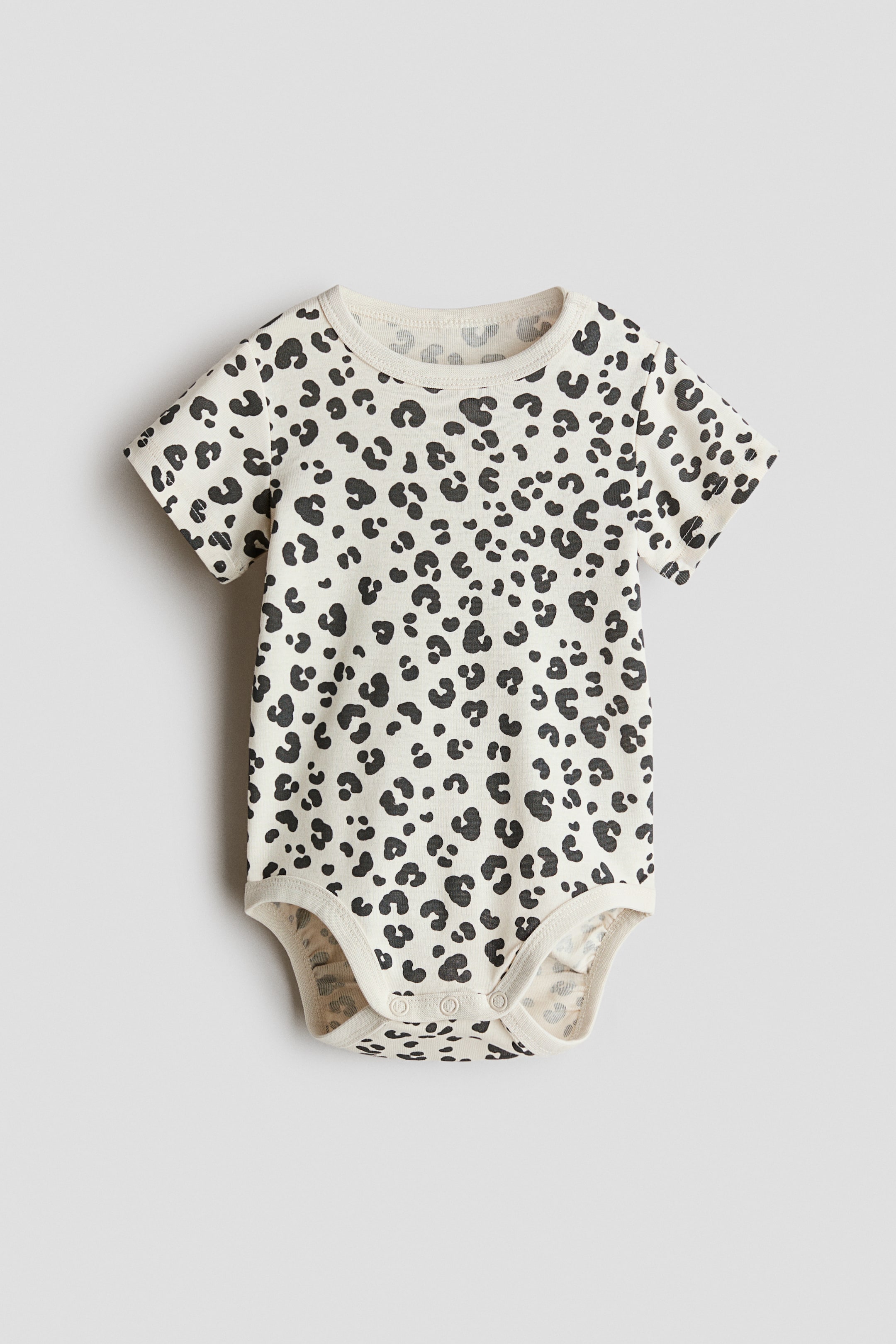 View larger image: This short-sleeved bodysuit, designed with a front-facing style, features a striking all-over black leopard print set against a cream backdrop. It showcases a round, ribbed neckline and includes convenient press-studs on one shoulder and at the crotch.