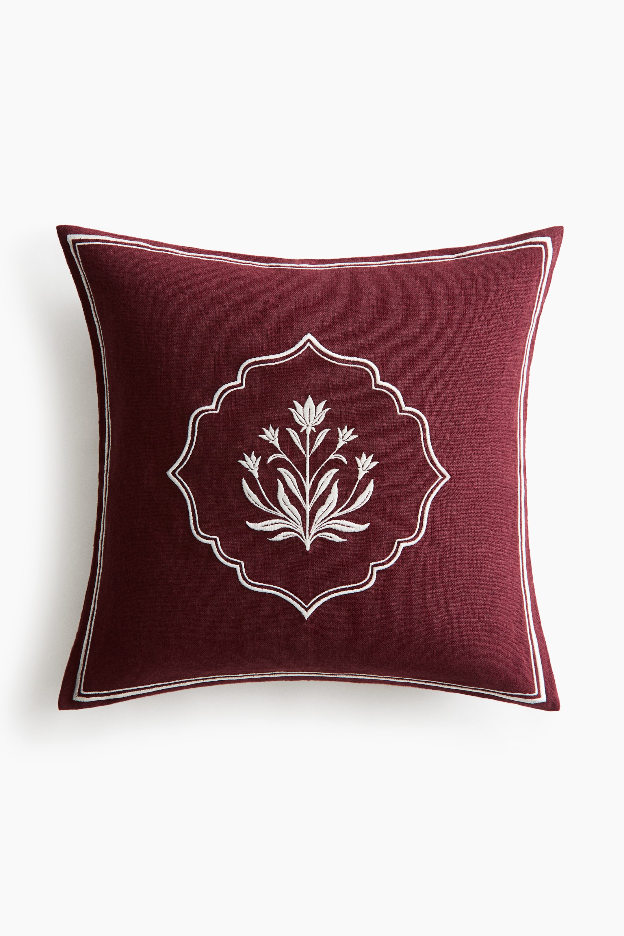 View larger image: A square burgundy cushion is shown front-on, featuring a central white embroidered floral motif enclosed within a scalloped frame. A thin, double-lined white embroidered border frames the outer edges of the cushion.