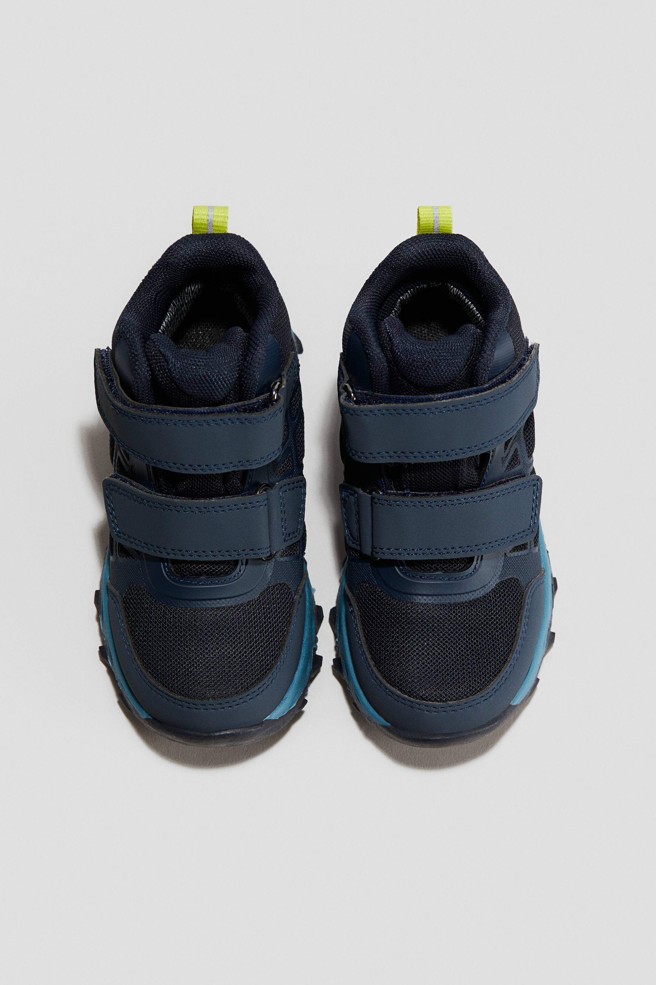 Visa större bild: Trackmid Wp 2v Stödjande, funktionell barnstövel. De två mörkblåa mellanhöga stövlarna är vända framåt, var och en med två kardborreband framtill. De visar upp meshpaneler på tån och sidorna, en robust mörkblå och teal sula, och en limegrön dragflik vid kragen.