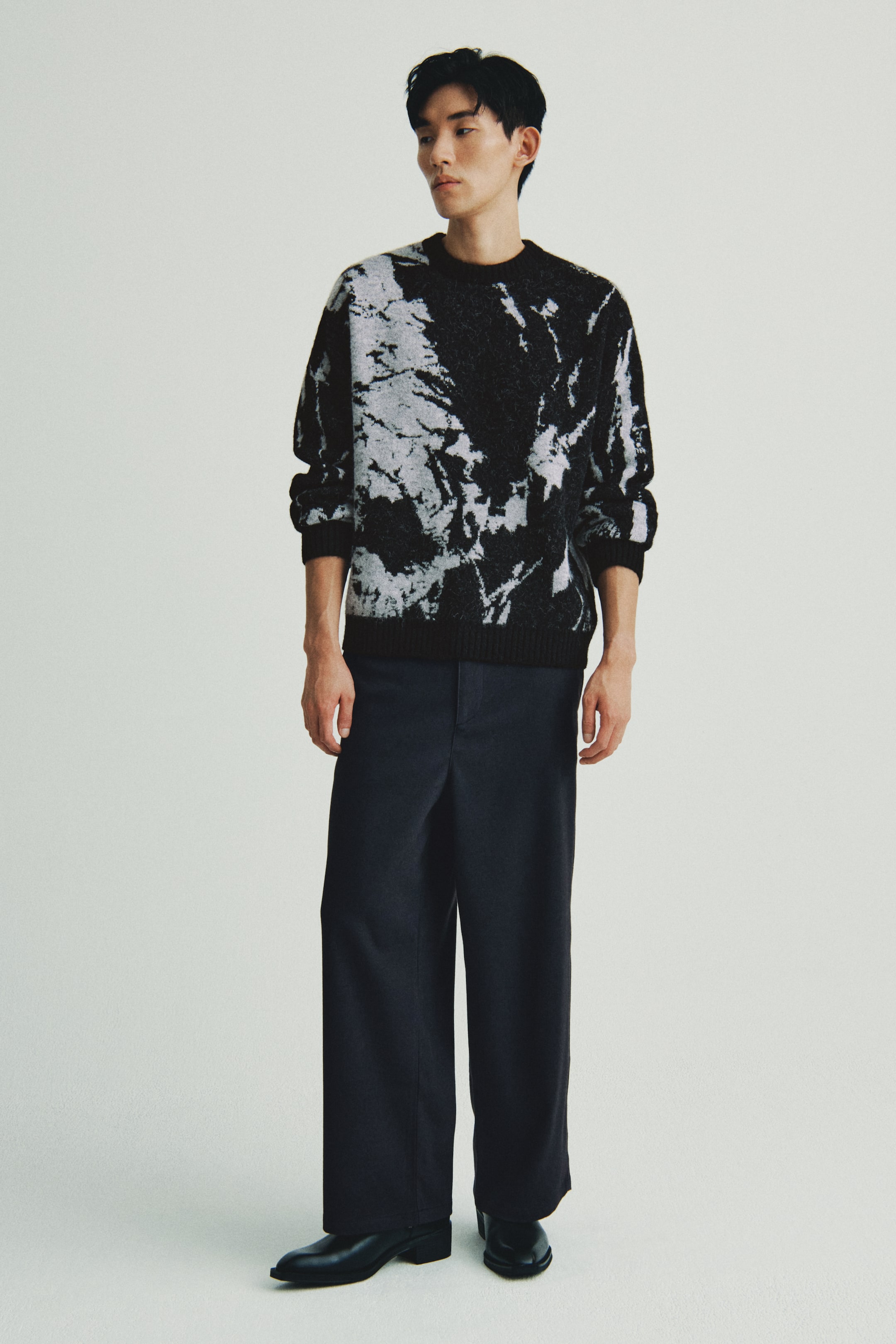 이미지 확대 보기: 블랙과 화이트 타이-다이 크루넥 스웨터는 리브드 커프스와 밑단이 특징이며, 정면에서 보이는 각도로 제시되고 있습니다. 다크 블루 와이드 레그 바지와 블랙 포인티드 토 슈즈와 함께 스타일링되었습니다.