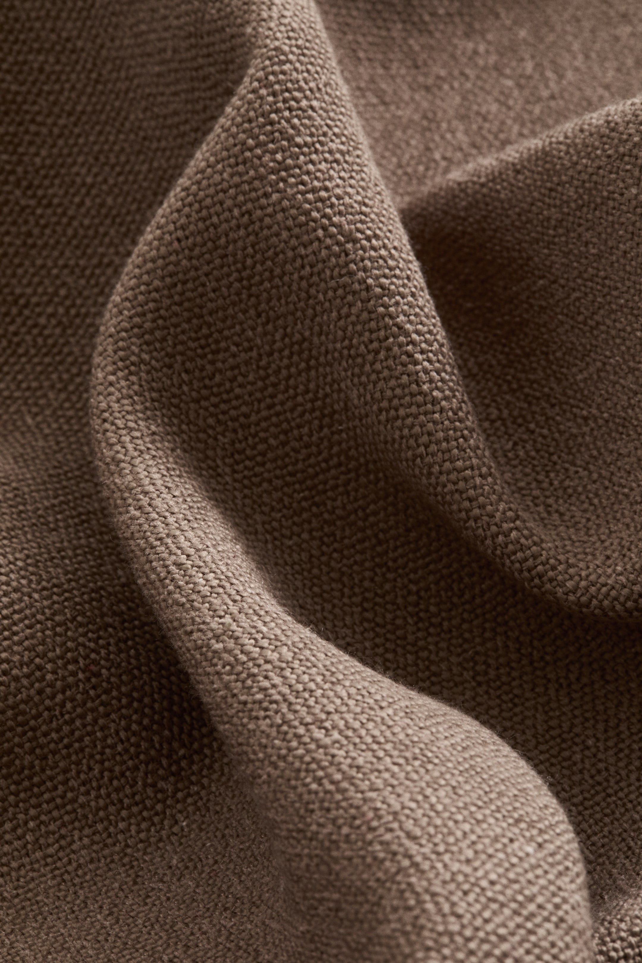 Agrandir l'image: Un lambrequin présente un tissage rustique, lourd et brun, affichant sa texture visible dans des plis doux.