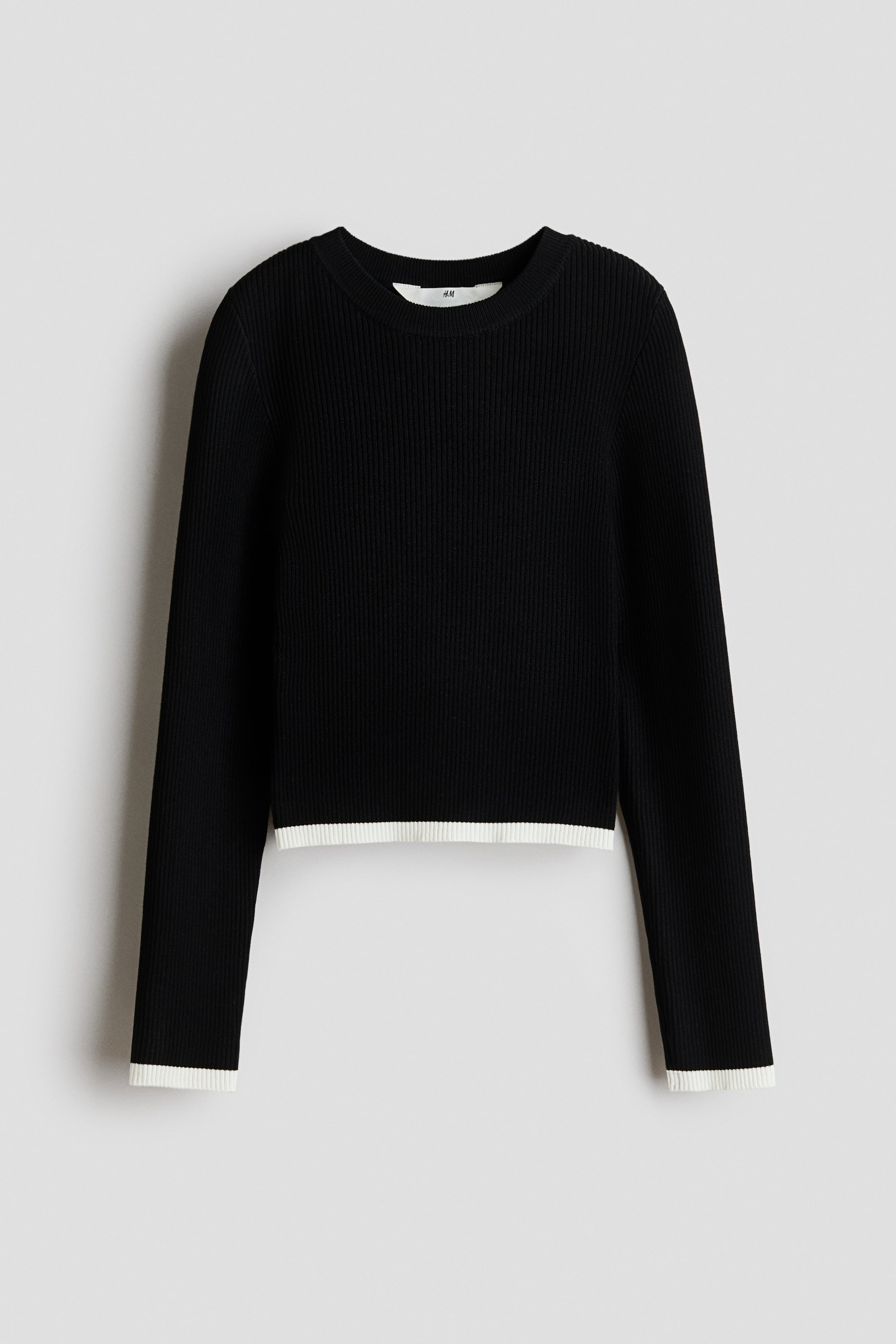 View larger image: A black ribbed knit long-sleeved top is displayed front-on, featuring a crew neck and white banding on its cropped hem and cuffs.