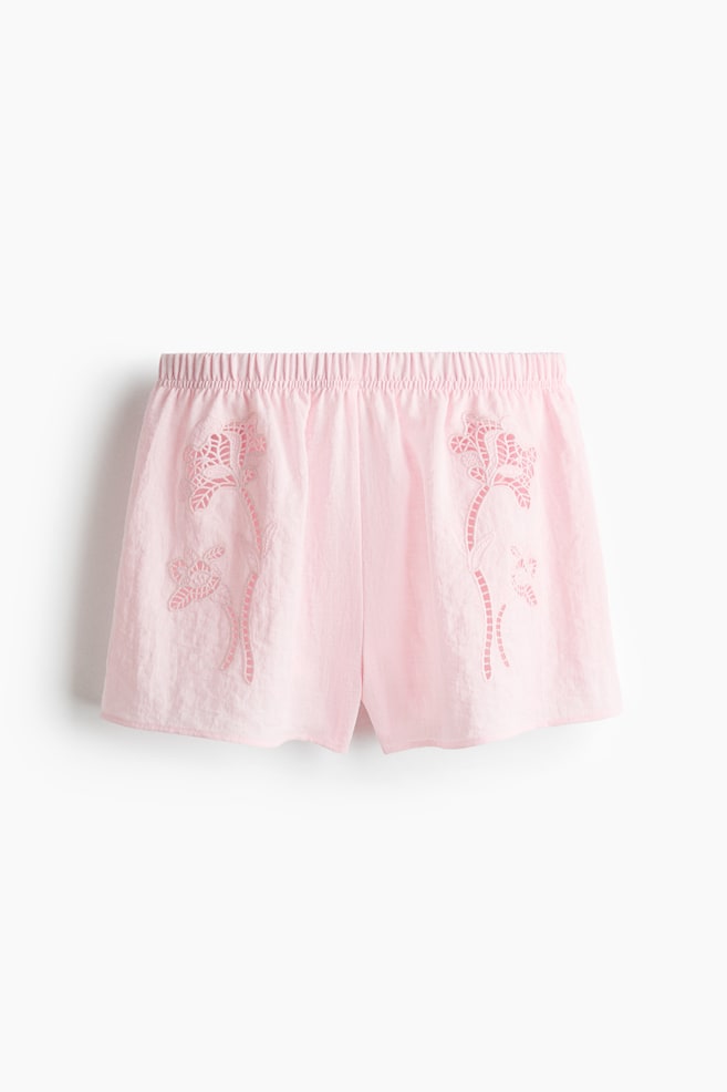 The pink shorts are displaying a loose fit and a regular, elasticated waist, with flower-shaped broderie anglaise decorating the front of the woven fabric. - 1